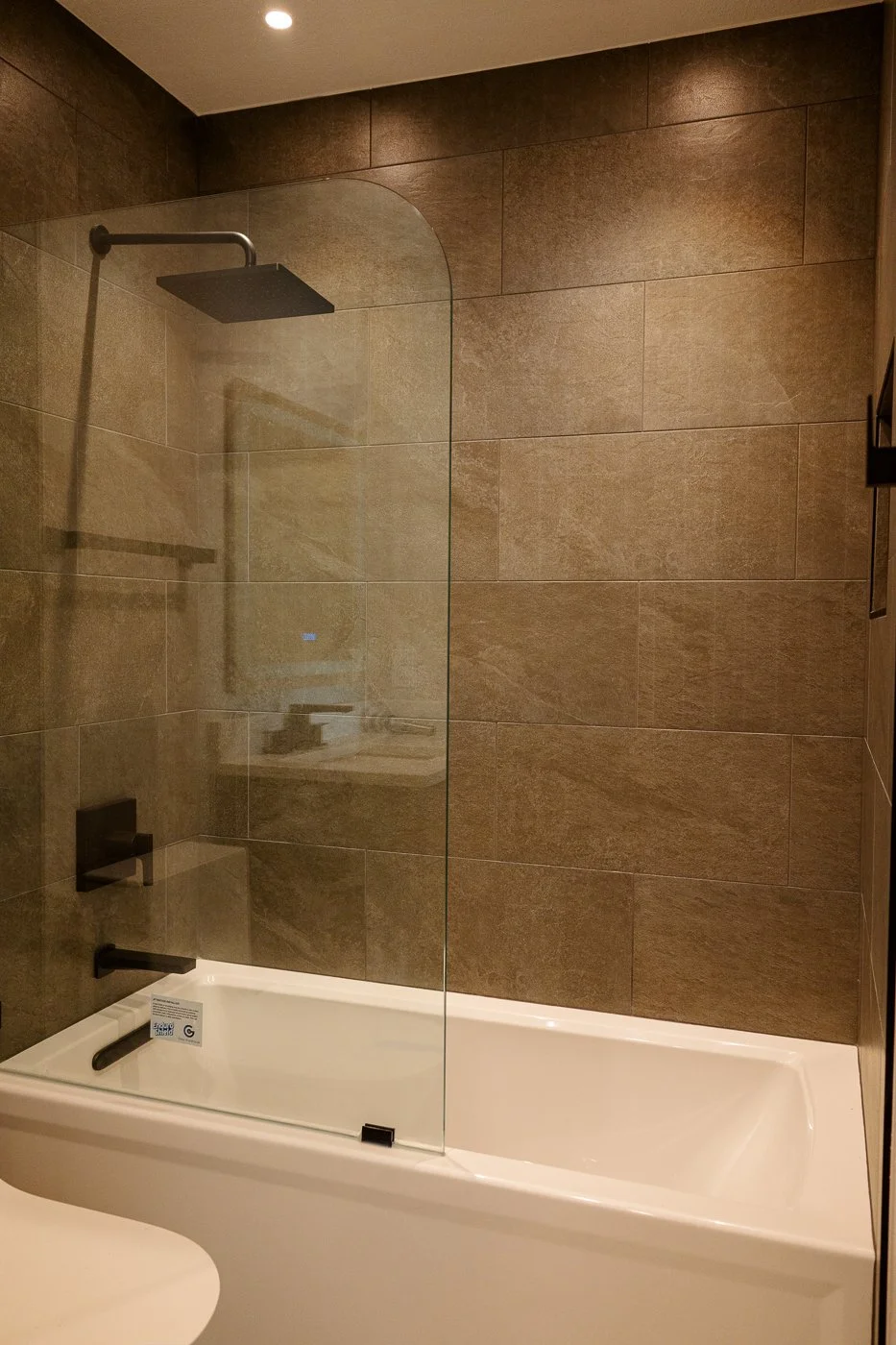 Bathroom with a bathtub, glass shower partition, dark brown tiled walls, and a mounted showerhead.