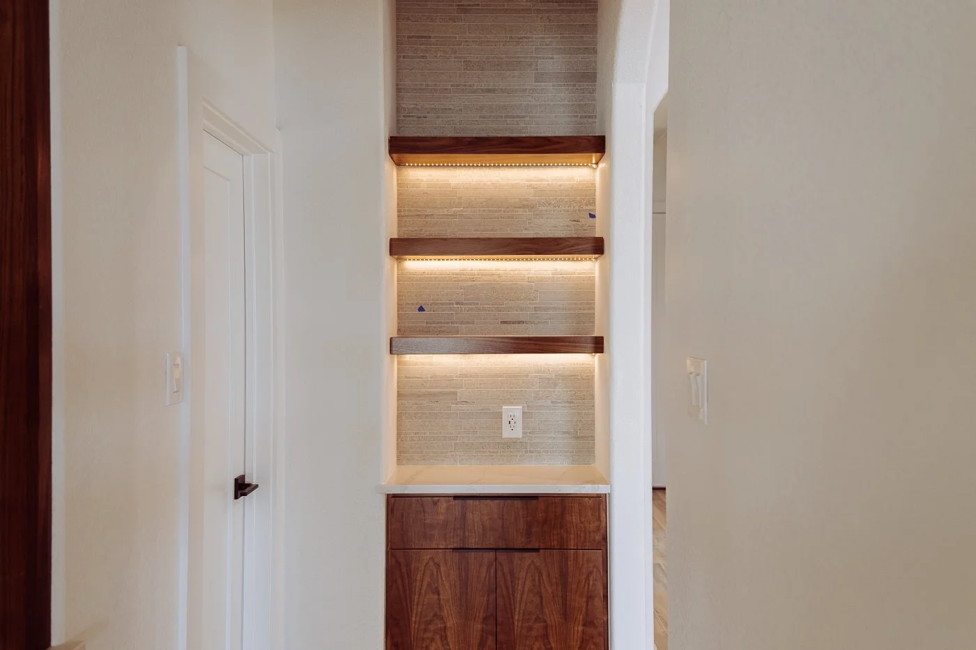 Built-in wooden shelves with LED lighting on a tiled wall, with electrical outlets below.