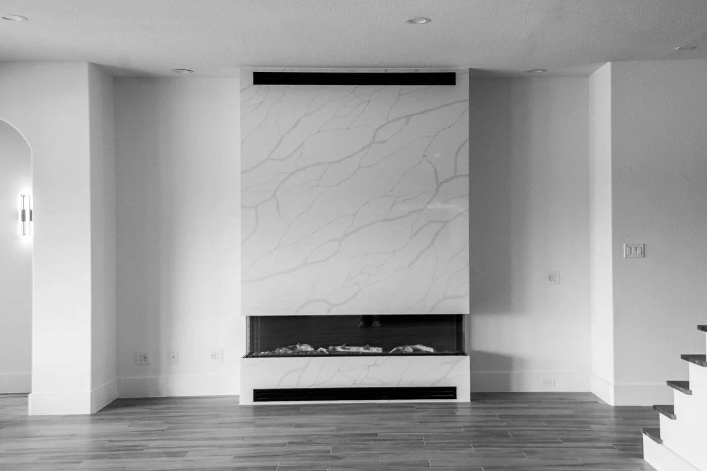 Modern living room with a fireplace with a marble surround, hardwood floors, white walls, and recessed ceiling lights.