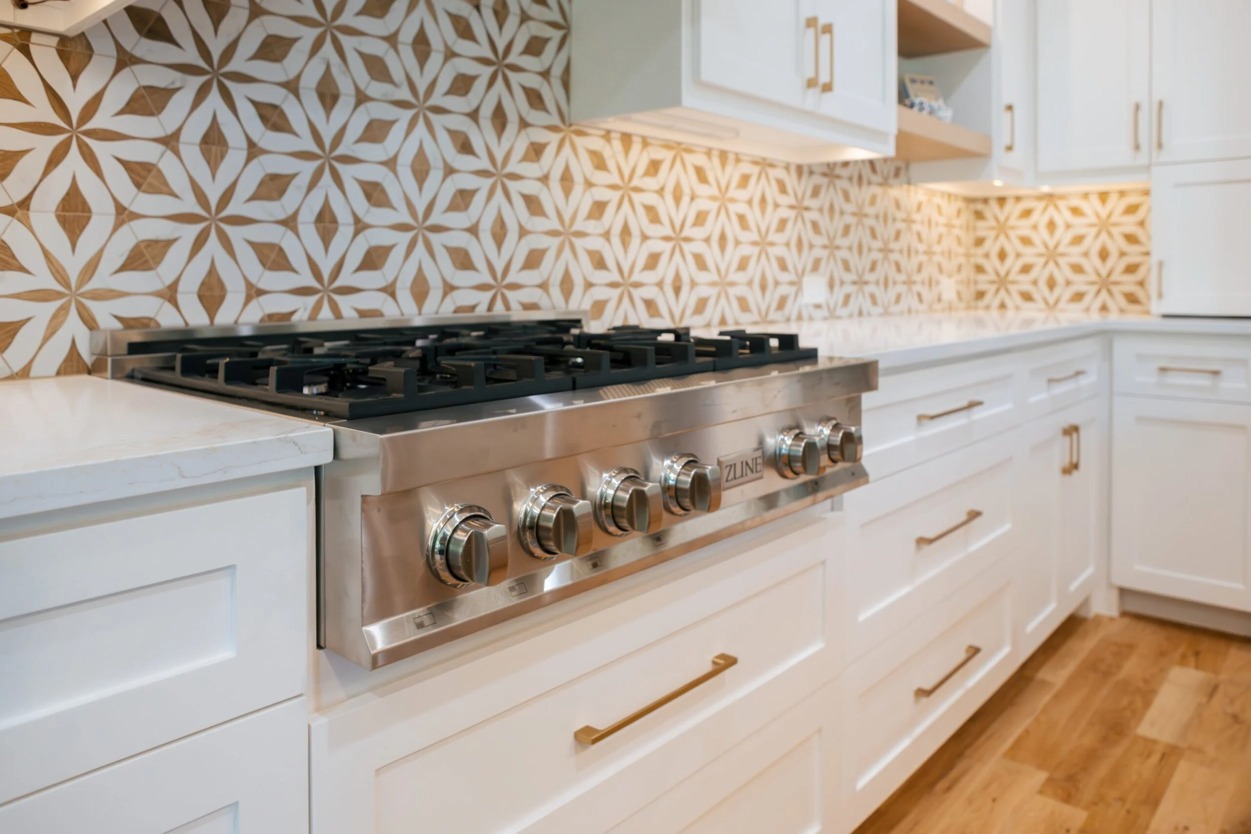 A modern kitchen featuring a stove with metallic knobs and a decorative tile backsplash with white and brown geometric patterns.