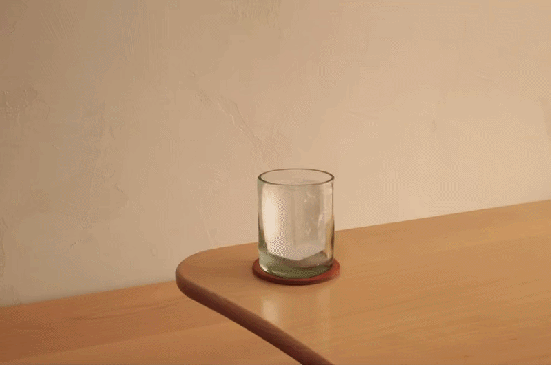 A glass on a wooden table with a thin stream of water dripping into it from above.