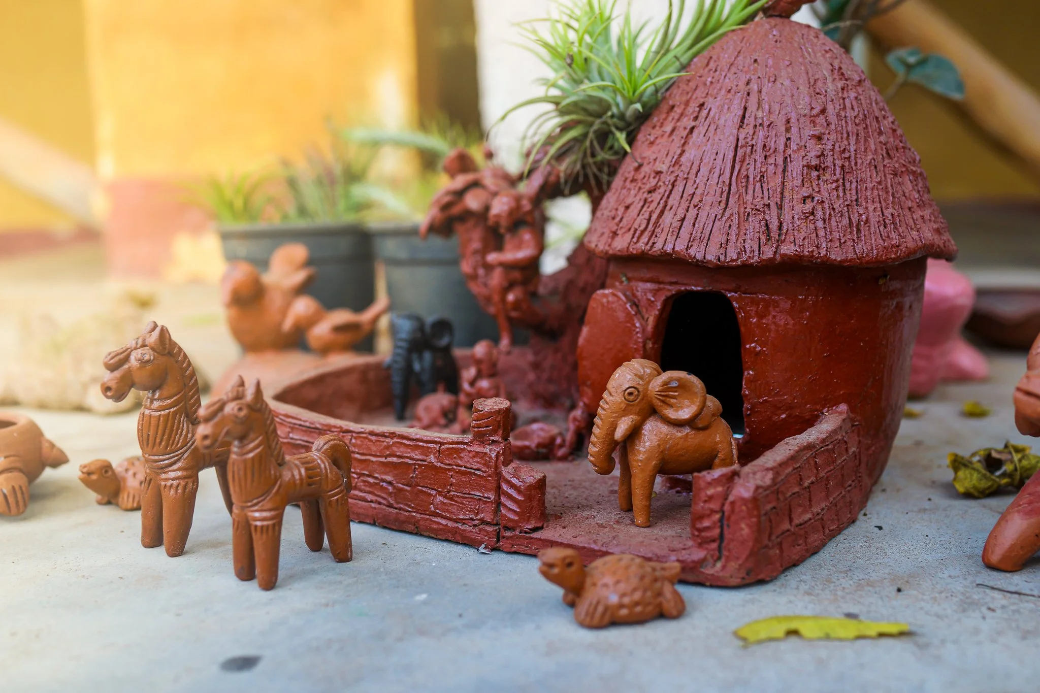Terracotta animal figurines and a house-shaped structure with plants on top, set on a flat surface.