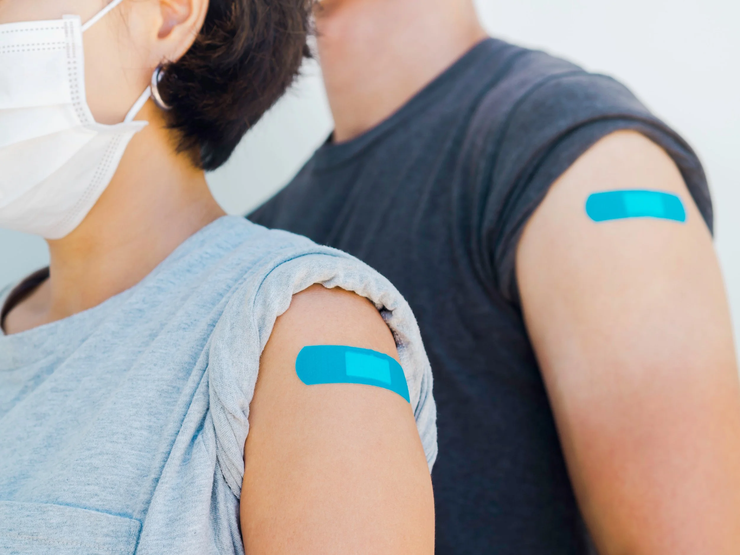 Two people with bandages on their upper arms after receiving vaccinations, close-up shot.