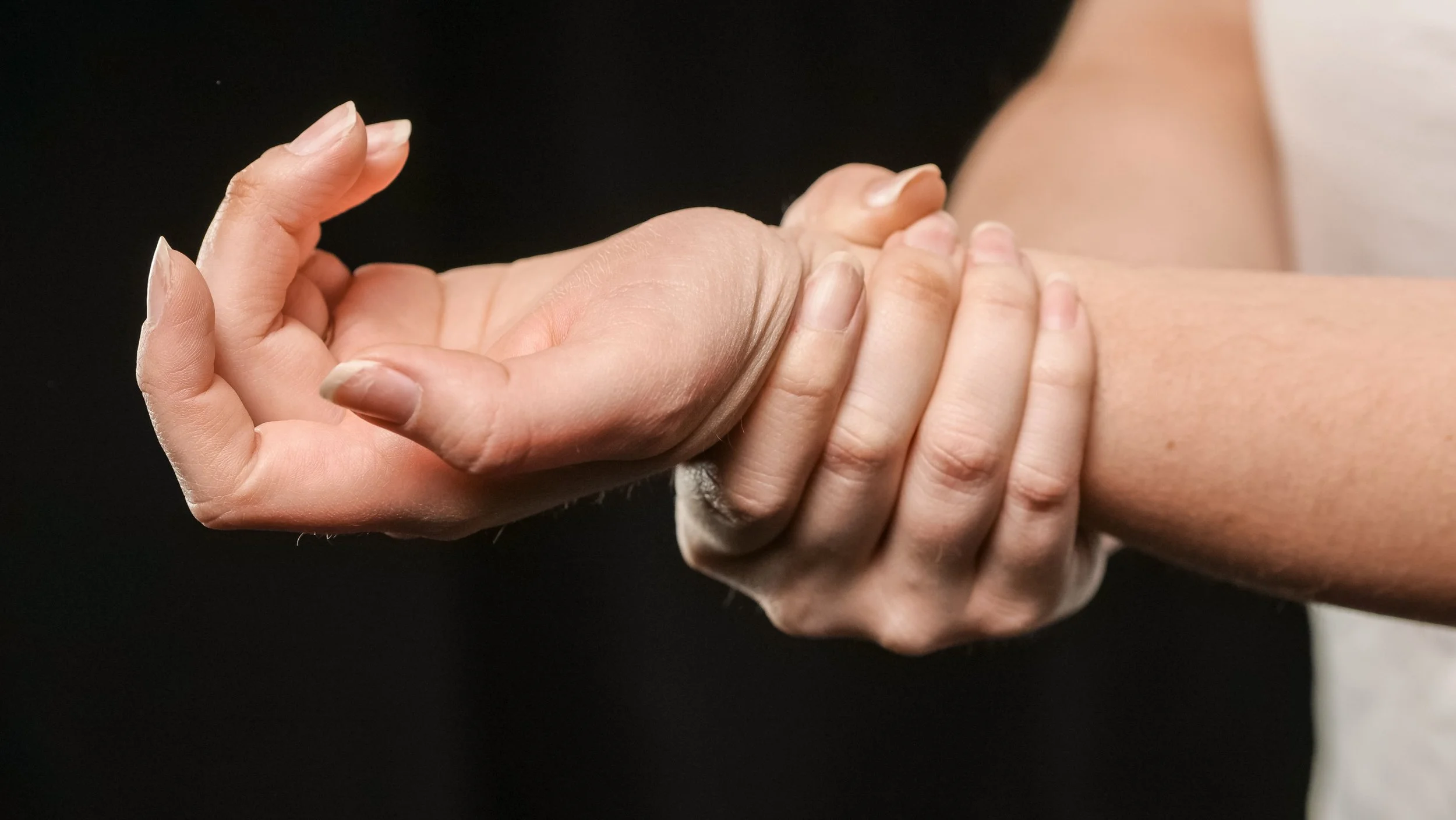 Close-up of one person giving a massage to another person, focusing on their hands and arms against a dark background.