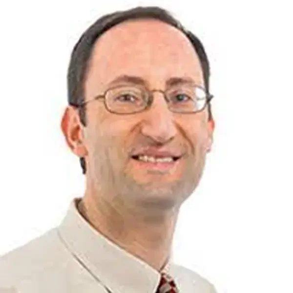 A smiling man with glasses, short dark hair, wearing a beige collared shirt, against a plain white background.