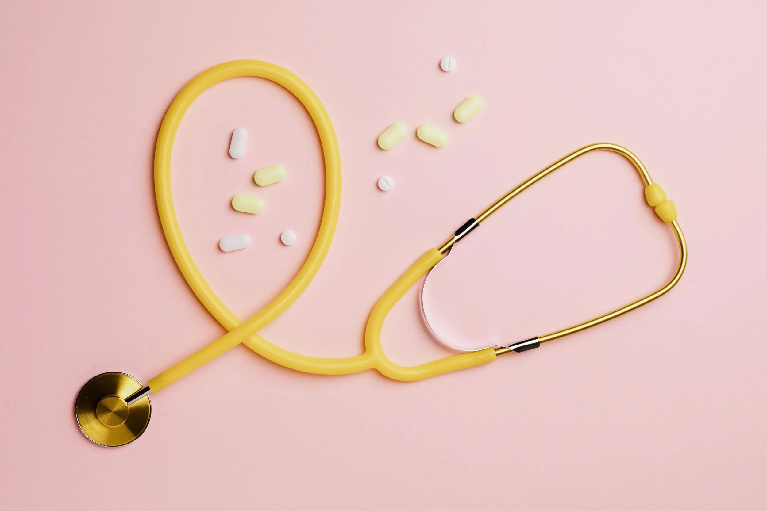 A yellow stethoscope with a pink background, scattered with white and yellow pills.