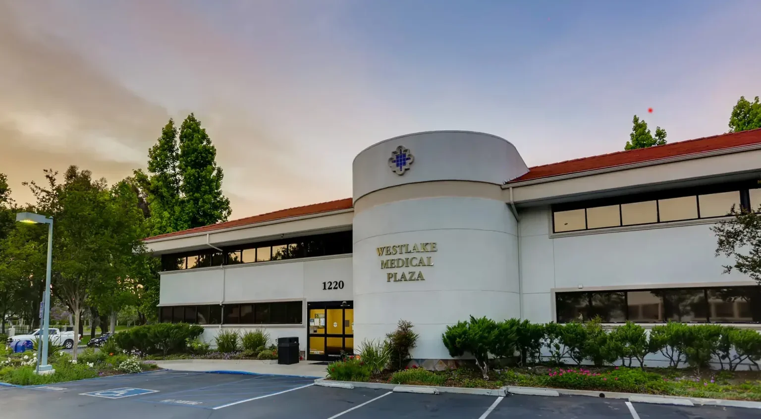 Exterior of Westlake Medical Plaza building with parking lot and surrounding greenery at sunset.