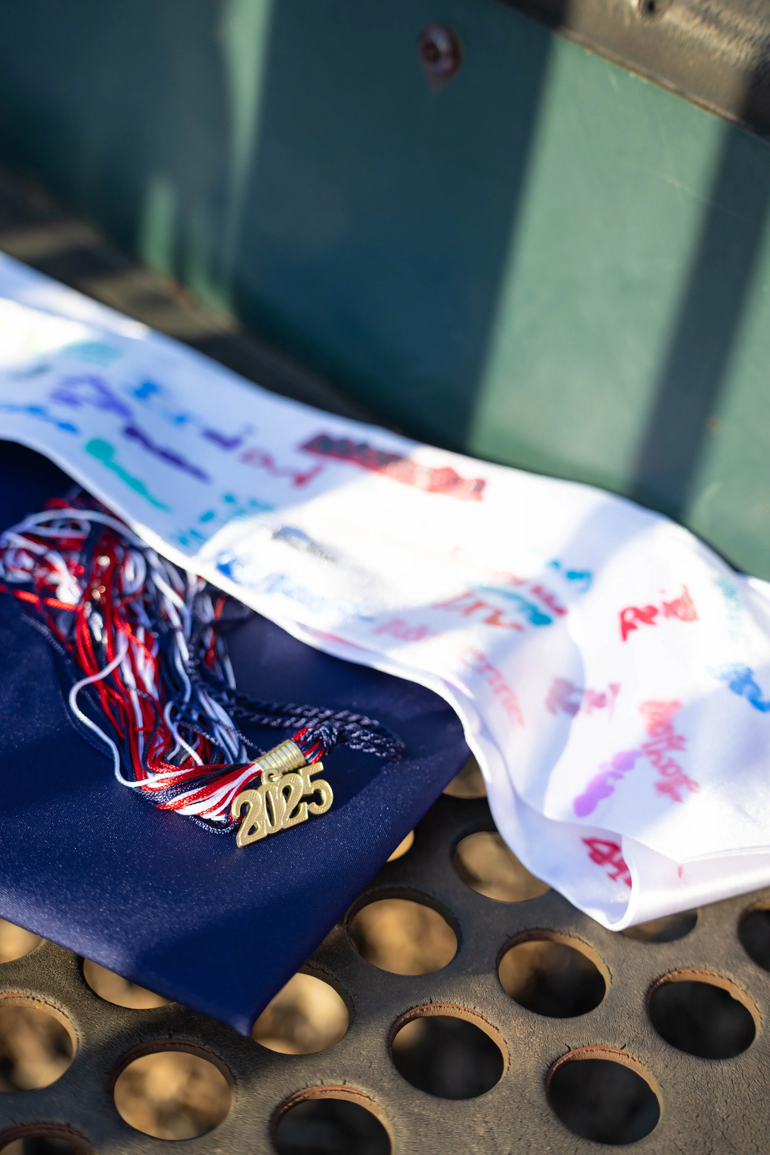 A pair of black sneakers with red, white, and black laces, a shiny gold medal with the year 2025, and a white ribbon with colorful writing and numbers, resting on a black perforated surface.