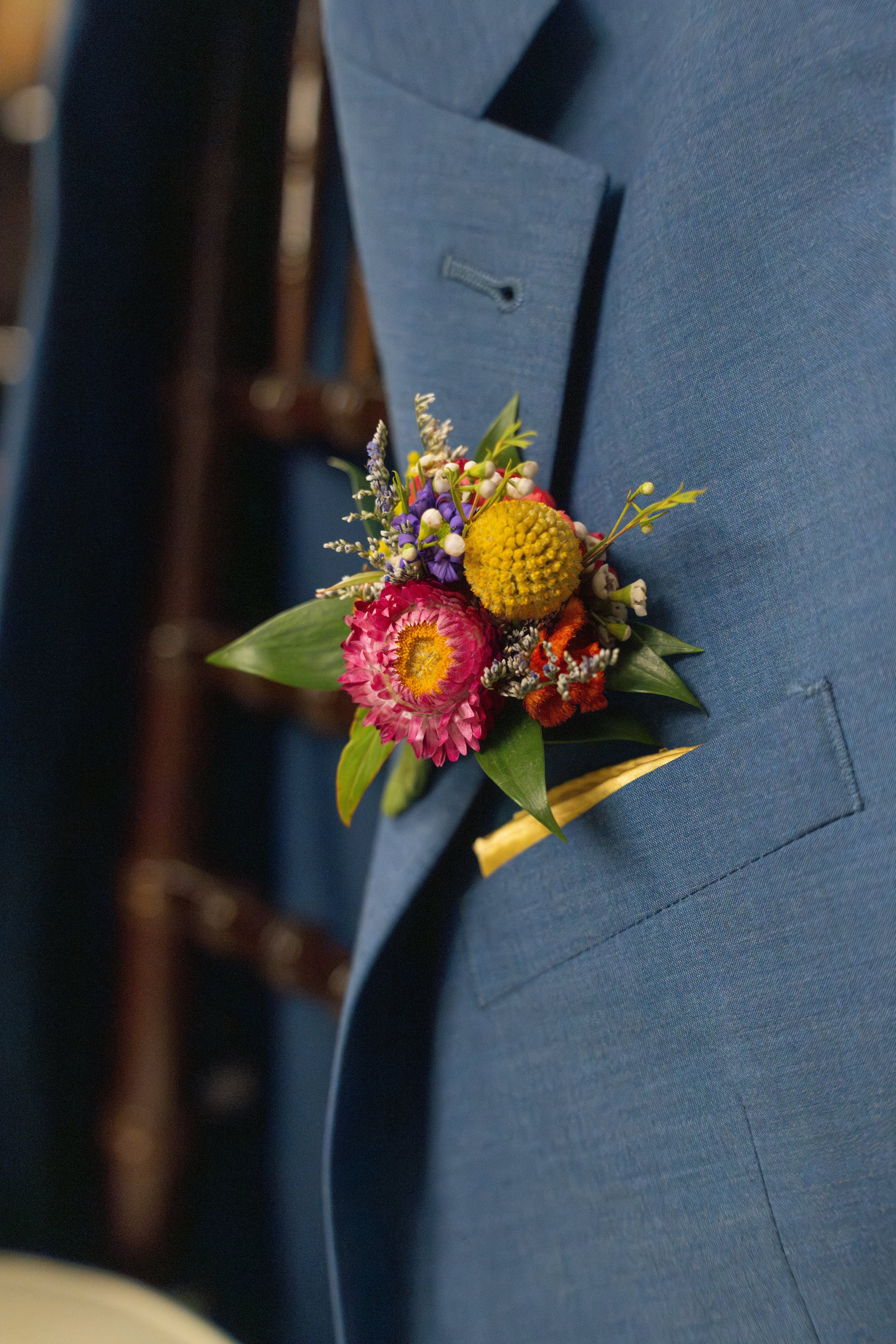 Close-up of a boutonniere with pink and yellow flowers, pinned to a blue suit blazer.