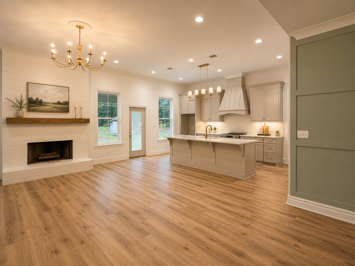 Open-concept kitchen and living area with hardwood floors, a white painted brick fireplace, a mantel with decor, large windows, a door leading outside, a kitchen island, white cabinets, a range hood, and pendant lighting.