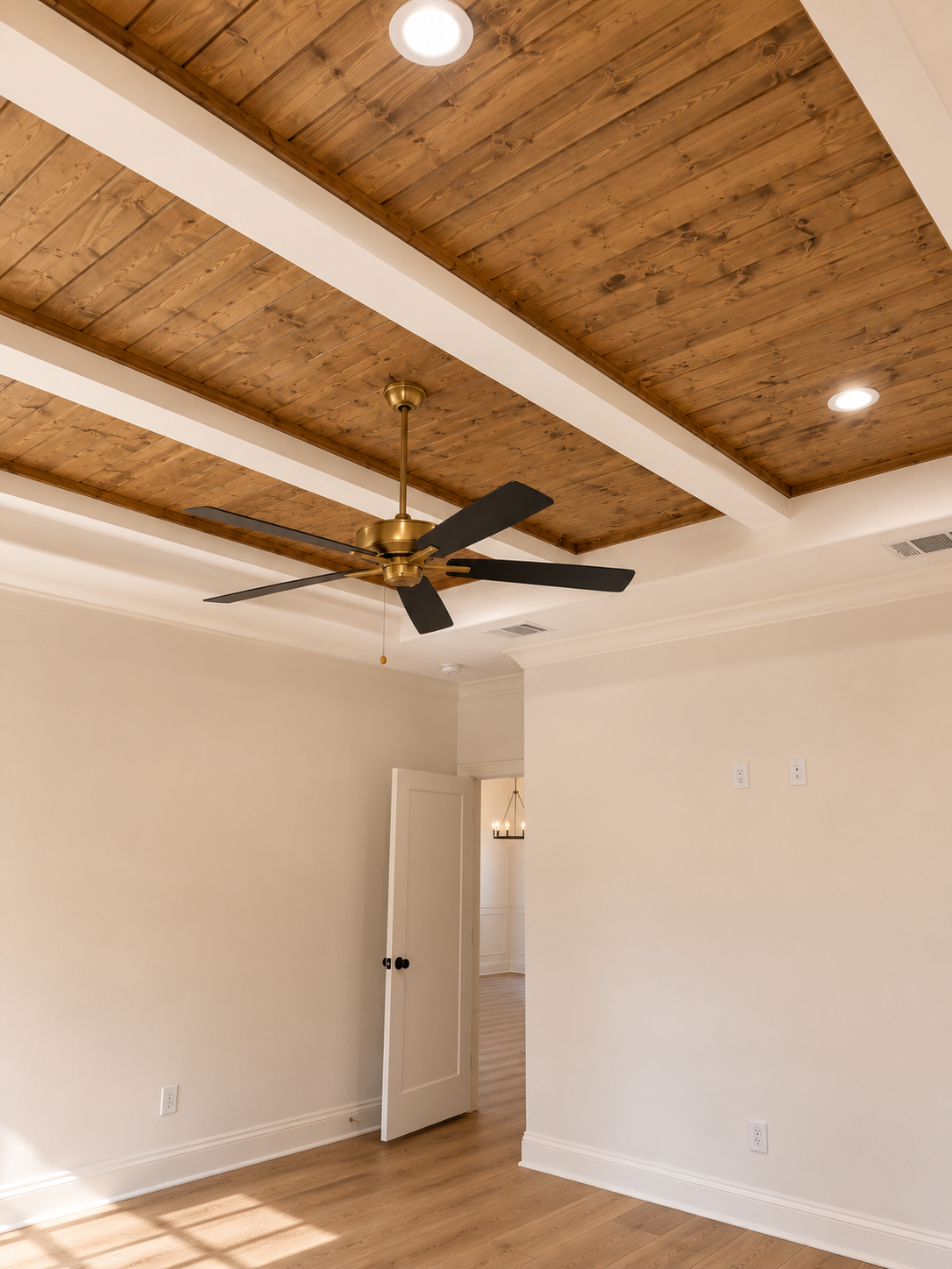 Empty room with wooden ceiling, ceiling fan, white walls, hardwood floor, and open door leading to another room.