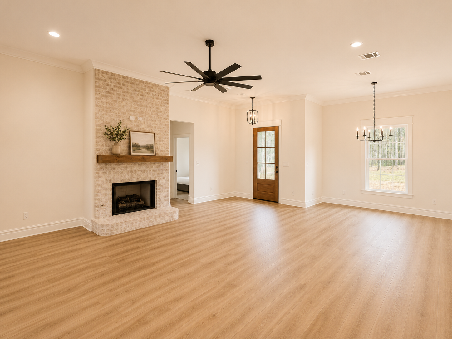 Empty living room with wood floor, brick fireplace, wooden mantel, and ceiling fans, with a window and door leading outside.
