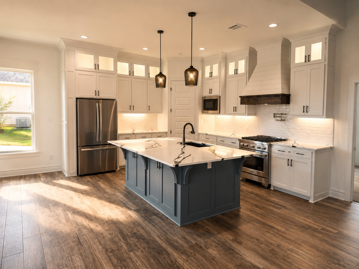 Modern white kitchen with an island, stainless steel appliances, white cabinets, and dark wood flooring, illuminated by pendant lights.