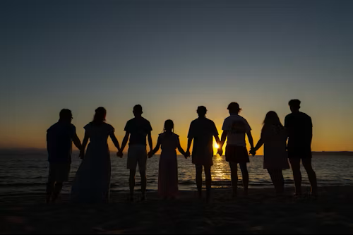 Group of eight people holding hands on the beach at sunset.