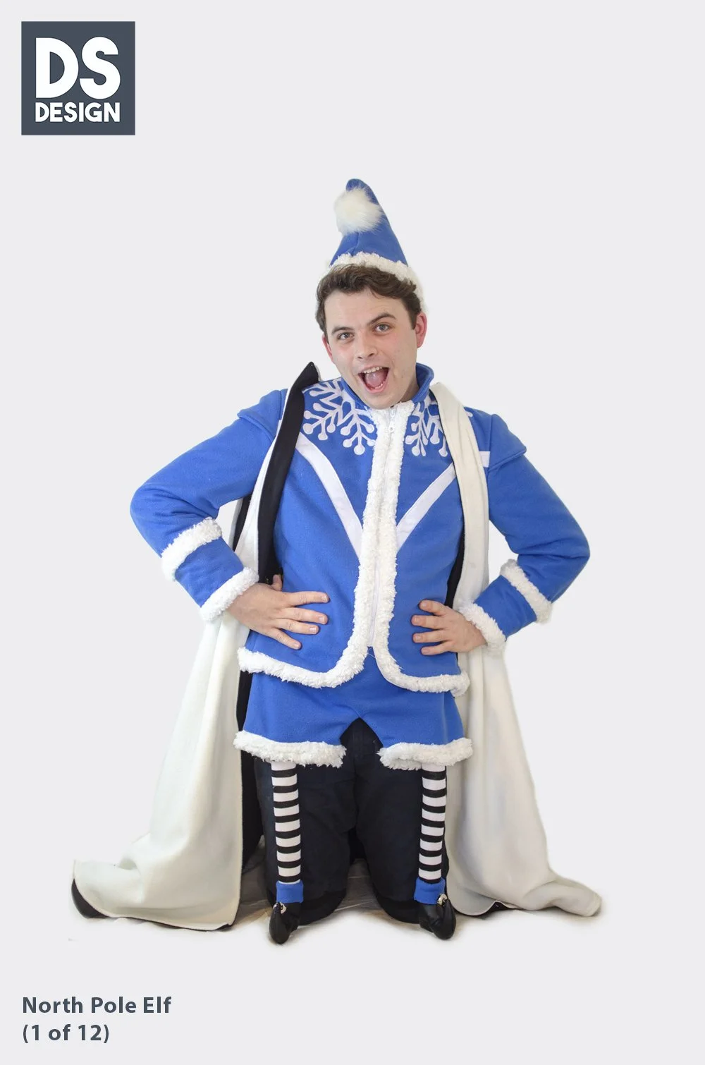 A person dressed as a North Pole elf standing with hands on hips, wearing a blue and white costume with striped socks, a pointy hat, and a white cape, smiling.