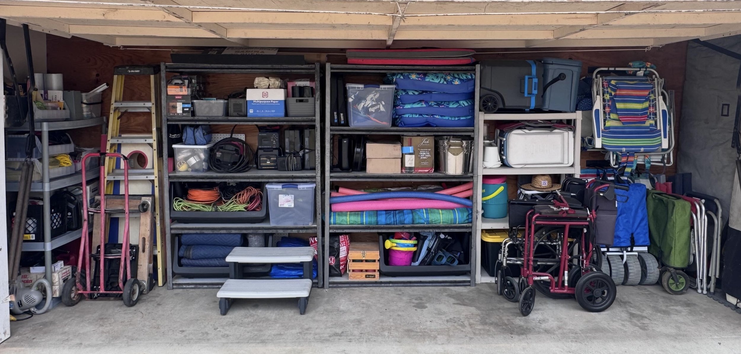 Organized garage shelves filled with household and outdoor items, including folding chairs, step ladder, yard tools, and storage bins.