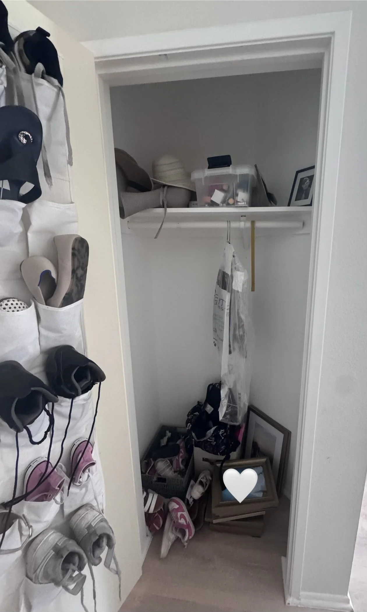 A closet with a shelf containing boxes and picture frames, with shoes and sandals on the floor and hanging organizers with shoes on the left side.