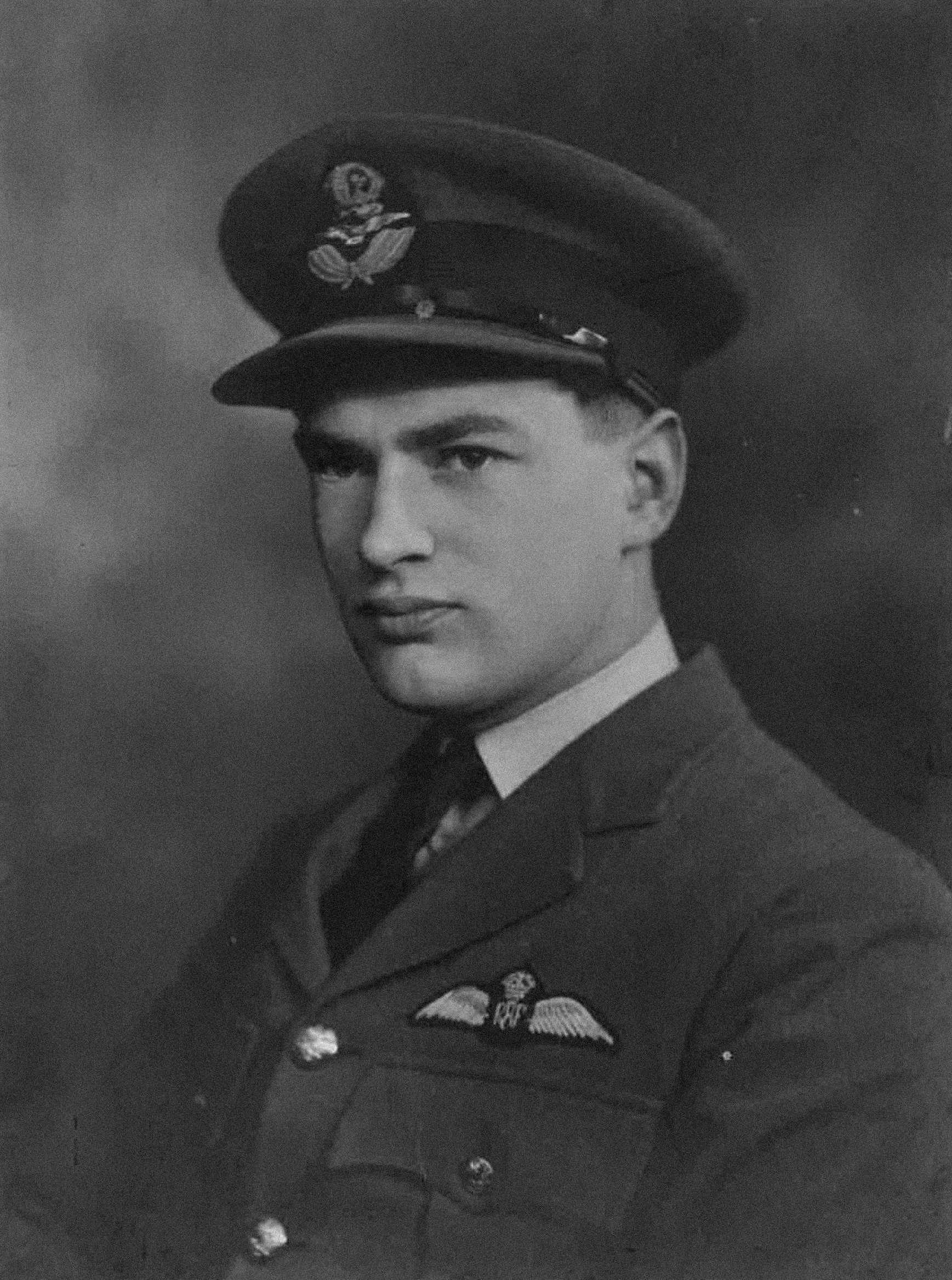 A black and white photograph of a young man in a formal military uniform, including a peaked cap with an insignia, a jacket with medals, and tie, looking slightly to the side with a serious expression.