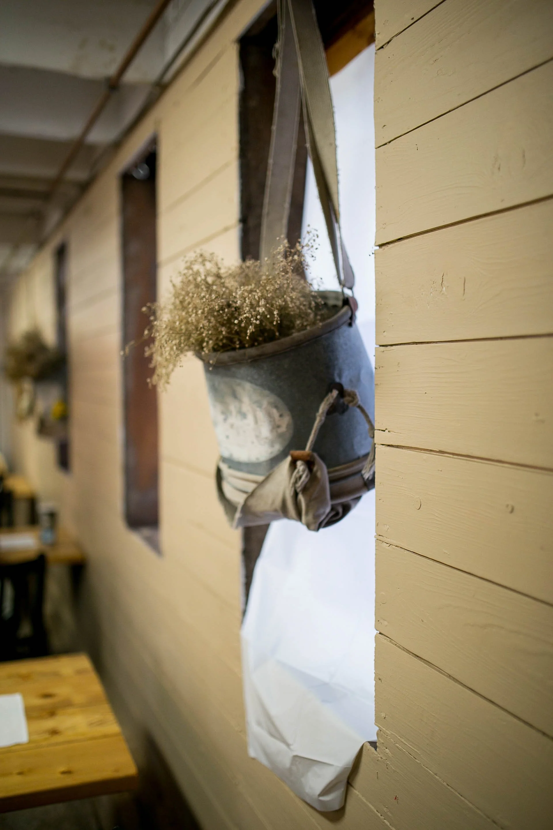 A small metal bucket holding white baby's breath flowers hanging on a wooden wall with a strap.