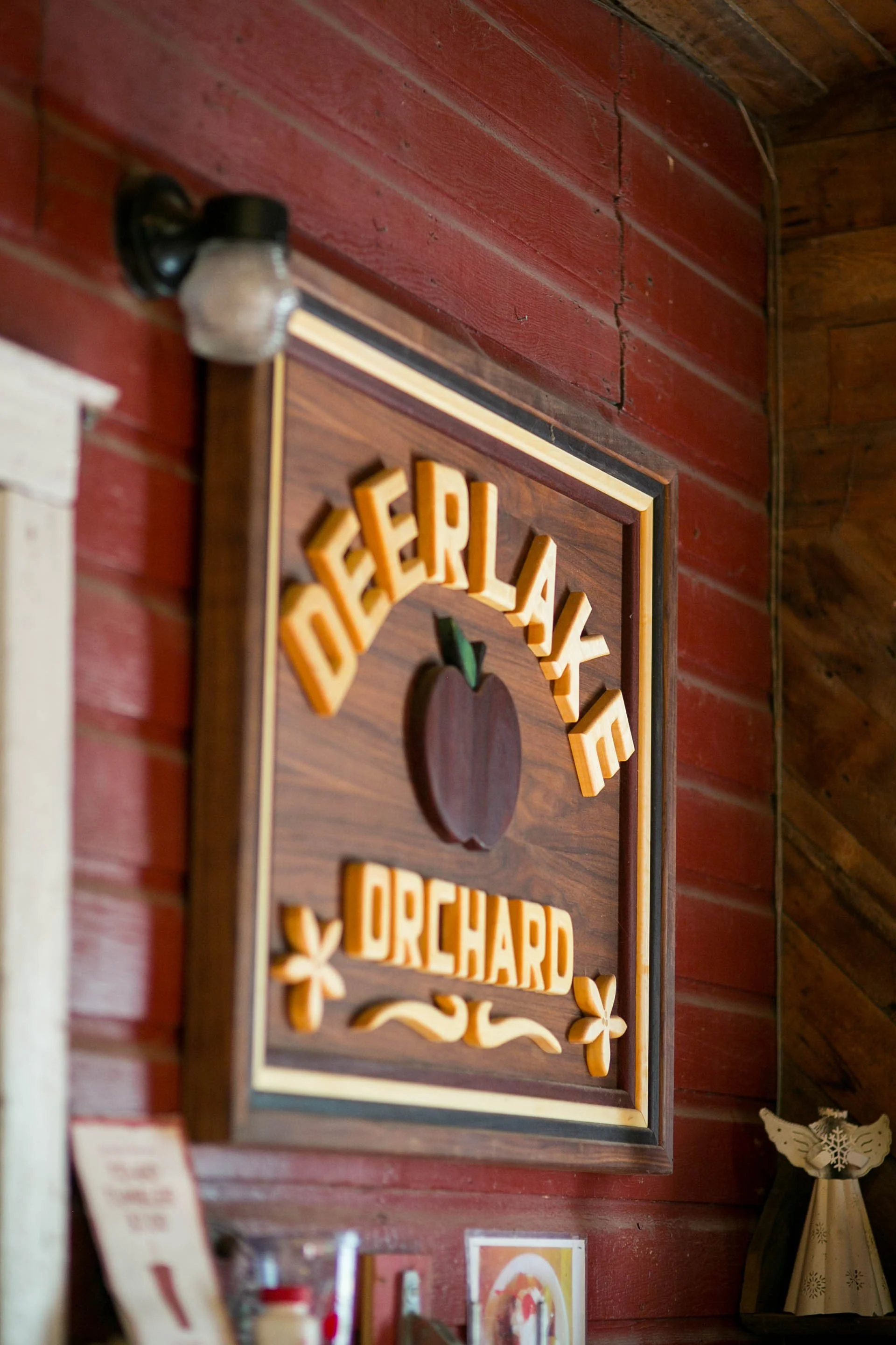 A framed decor piece with the words 'Dinner & Cheer' in raised yellow lettering, decorated with hearts and stars, hanging on a red wooden wall.