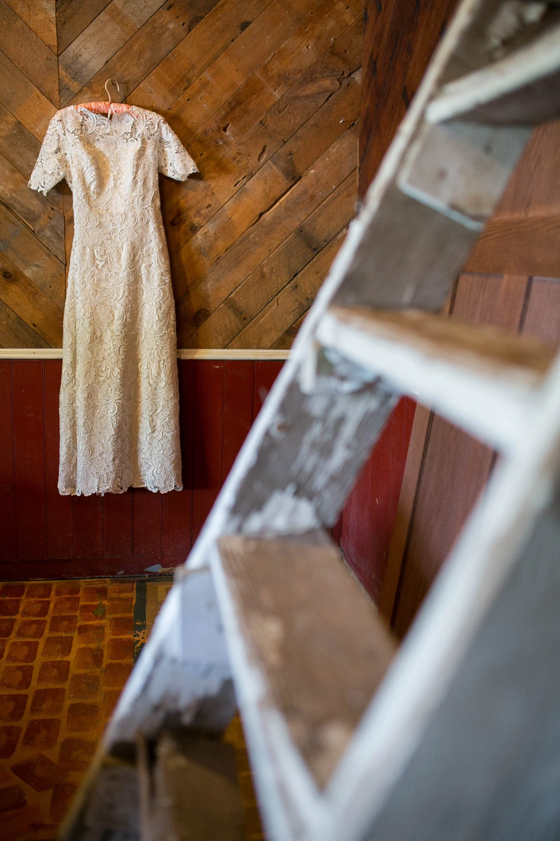 A white lace dress hanging on a wall with wooden paneling, viewed from above through a staircase railing.