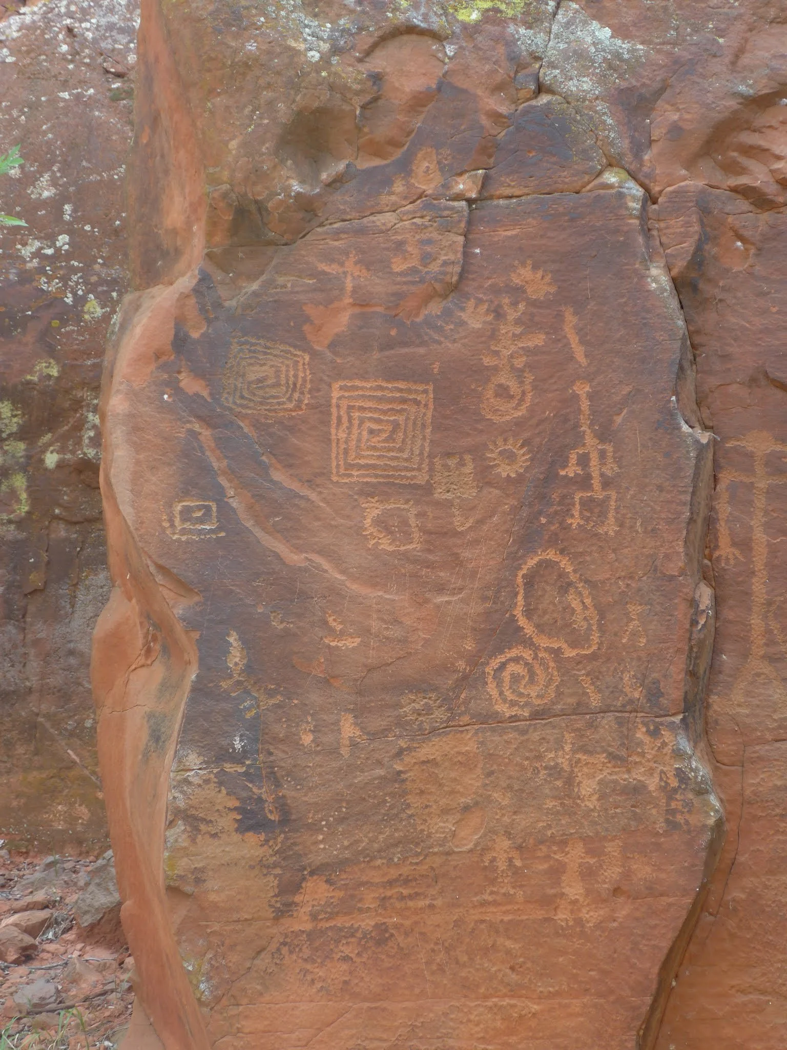 Red rock surface with ancient petroglyphs etched into the stone, including geometric shapes, spirals, and figures at the Crane Petroglyph Heritage Site in the Coconino National Forest southeast of Sedona, Arizona.