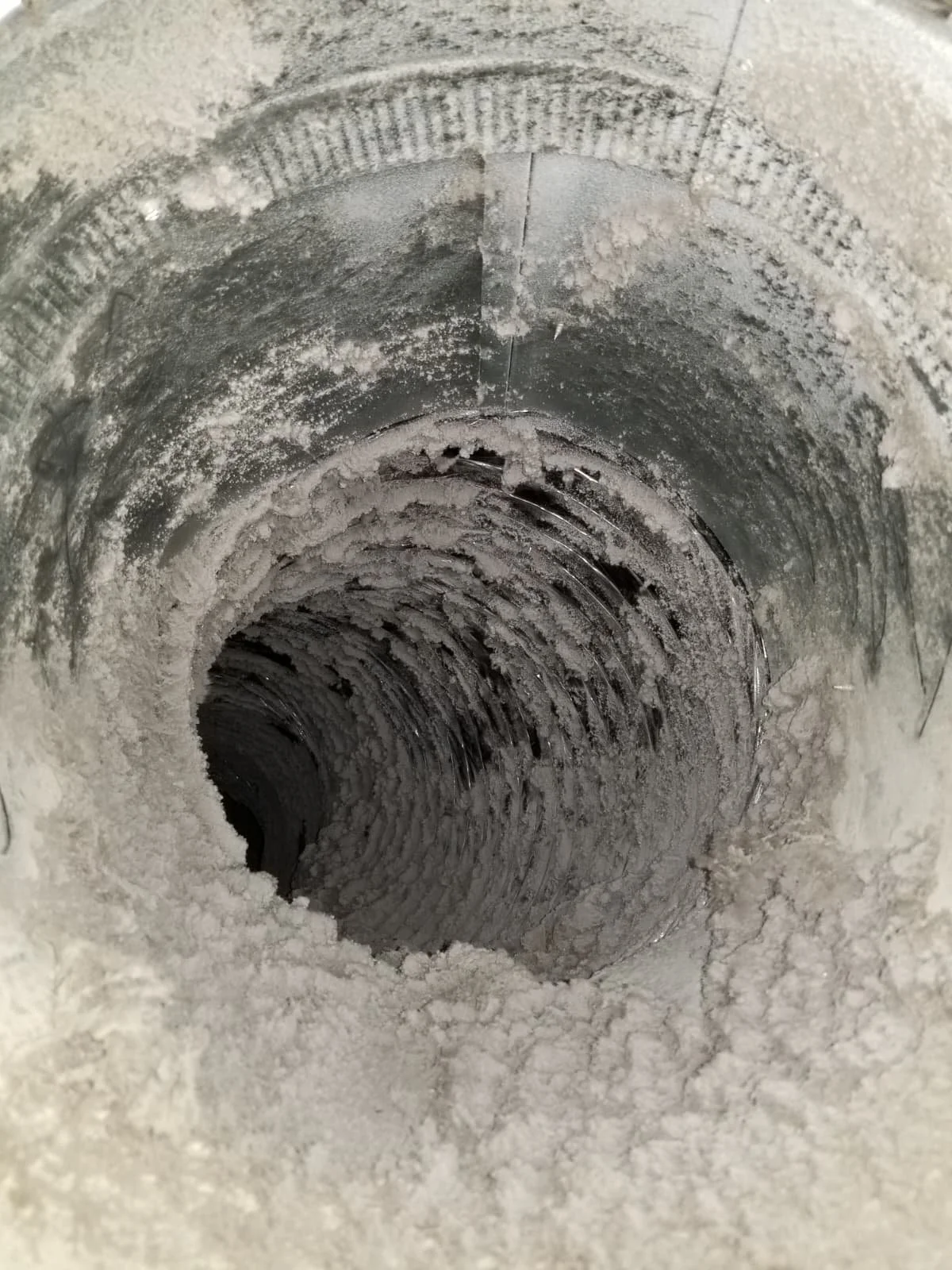 A close-up view of a circular metal pipe with a hollow interior, coated with a layer of white dust or powder.