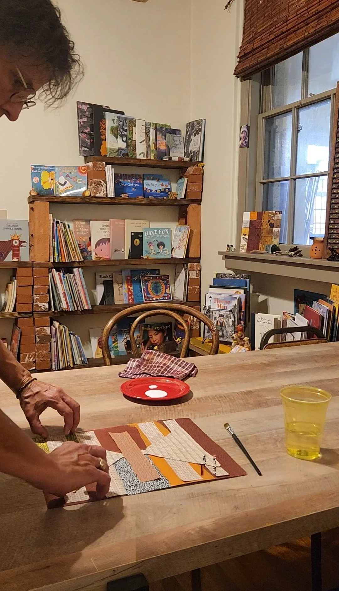 A person working on her next piece at a wooden table in her studio and nonprofit library.