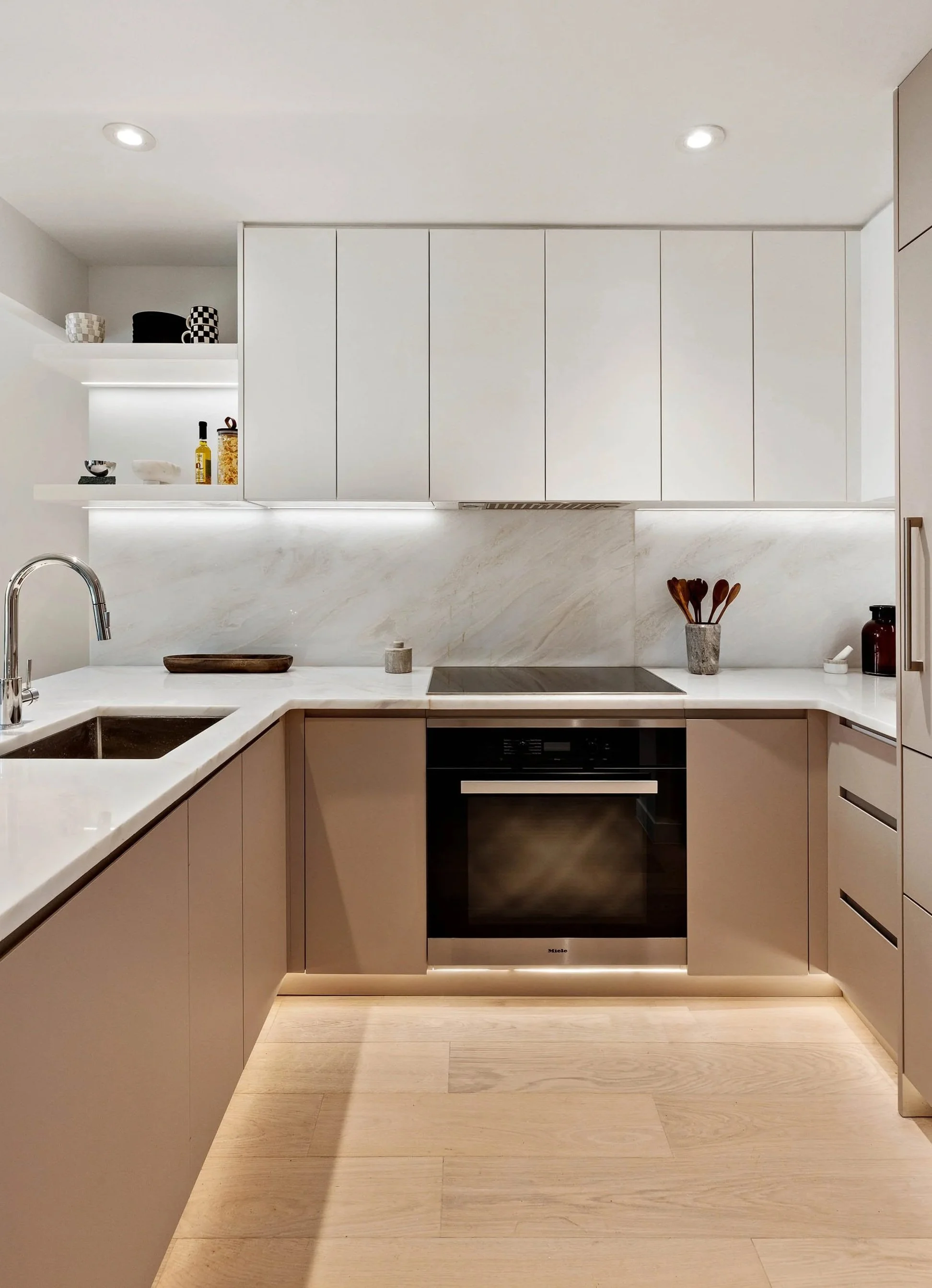Modern kitchen with white cabinets, marble backsplash, built-in oven, and light wood flooring. Developed by Ten Talents Management.