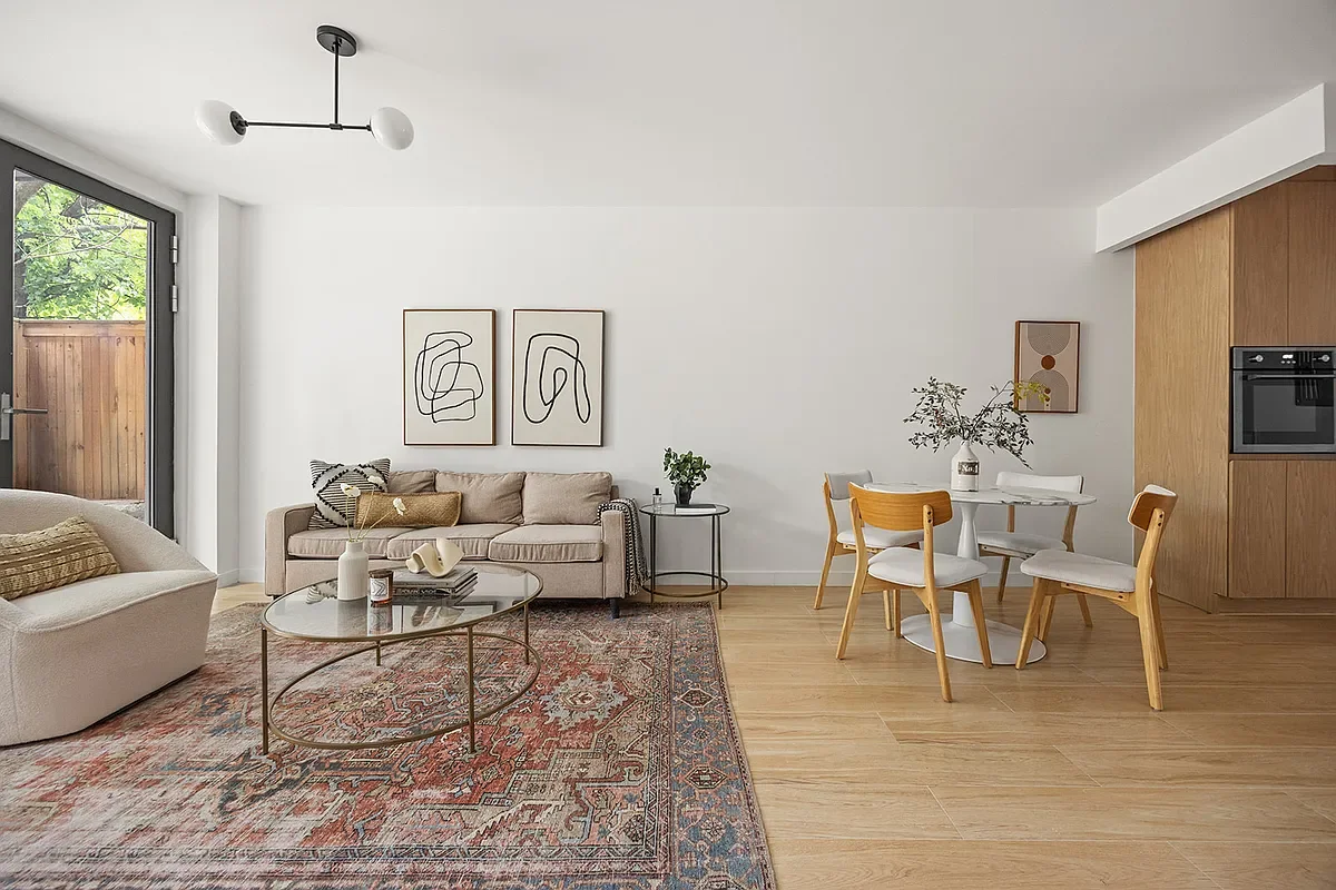 Living room with beige sofas, glass coffee table, patterned rug, wall art, and dining area with four chairs, a round table, and wooden accents. Developed by Ten Talents Management.
