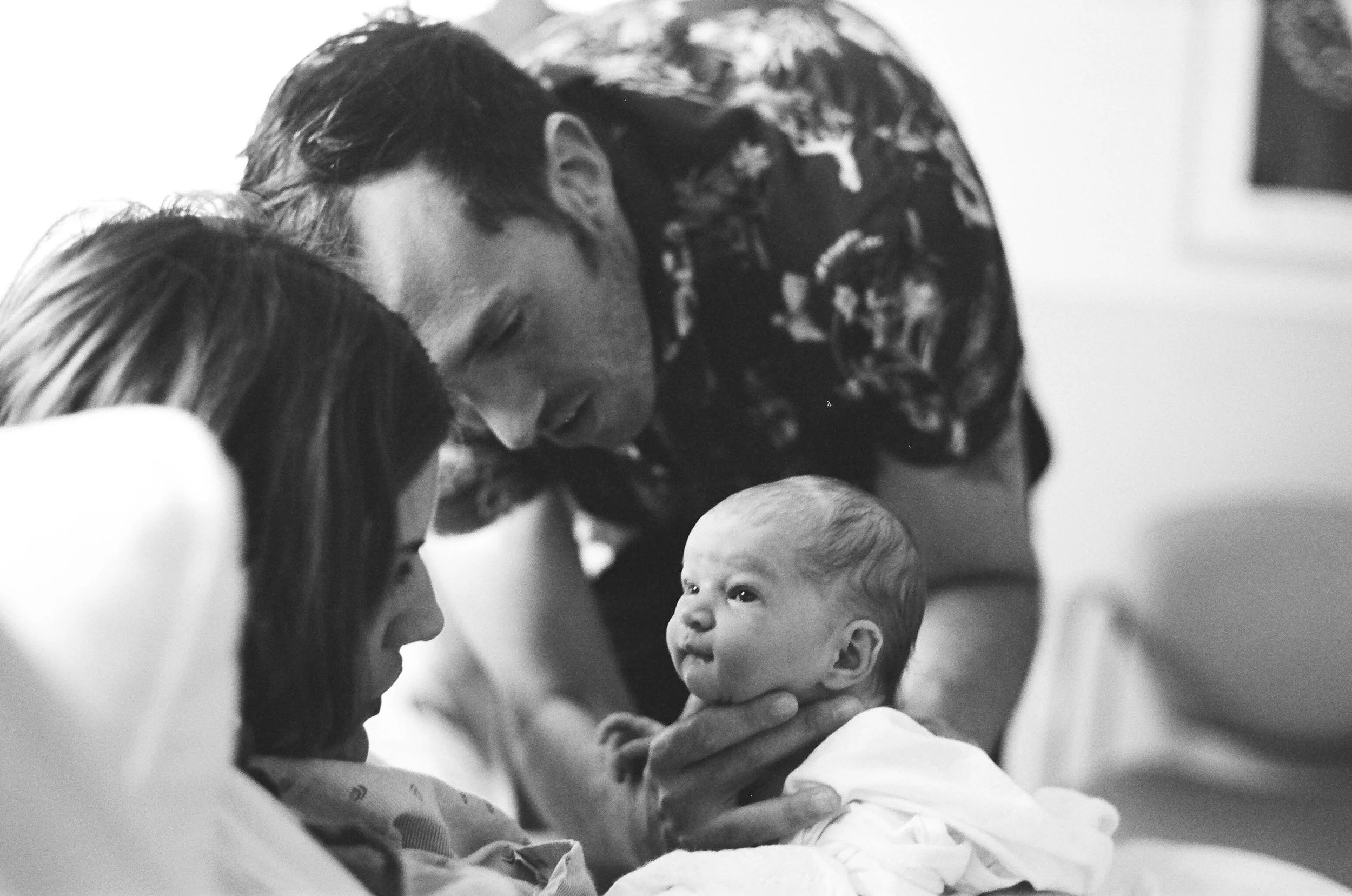 A woman, a man, and a young girl are close together, smiling and looking into the eyes of a small baby, creating a loving and happy family moment.