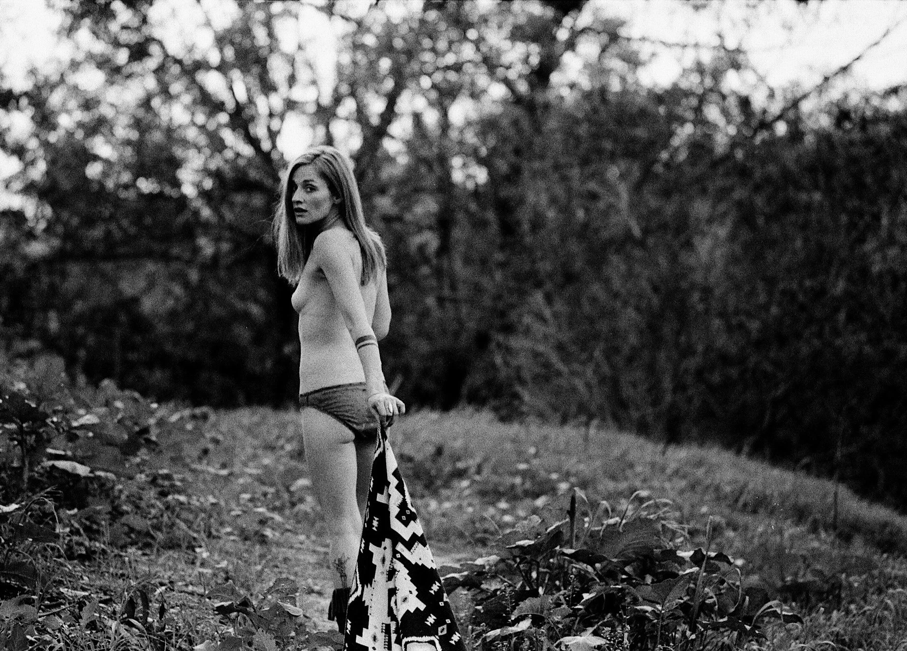 A young woman gazes back into a wooded area. 