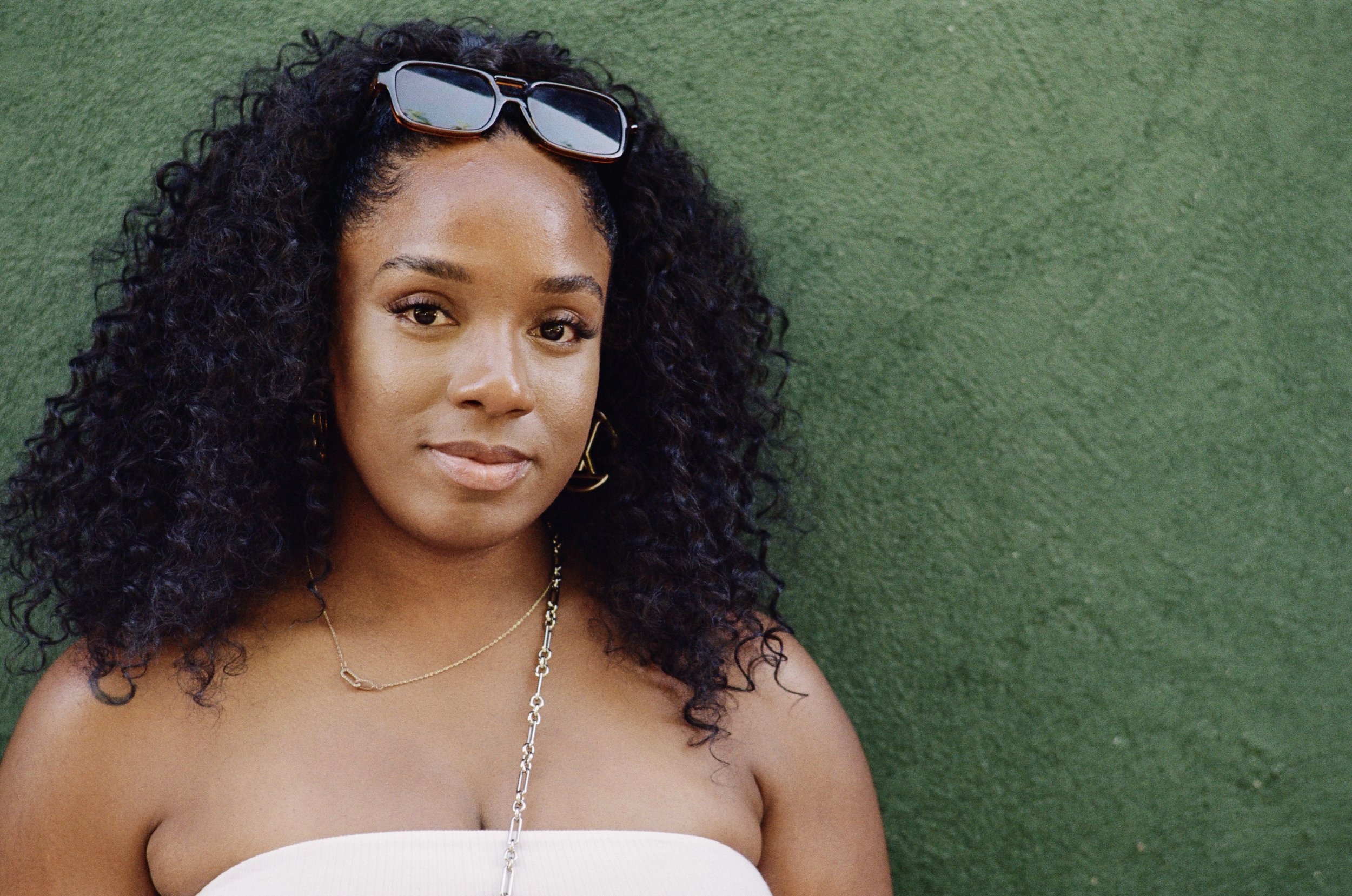 A stunning Black woman with curly hair is wearing sunglasses on her head. 
