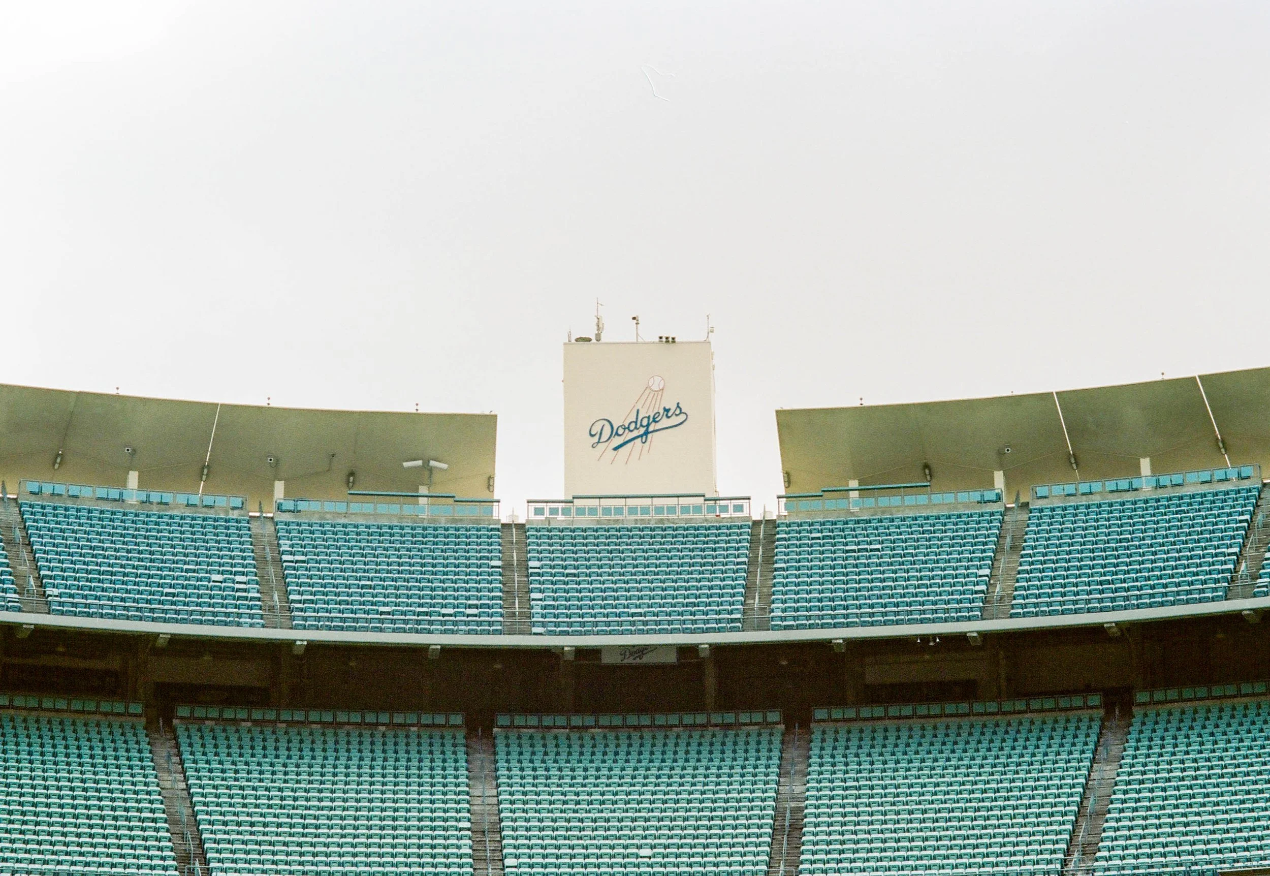 View of Dodger Stadium seating area with blue seats and the Dodger logo on a large sign in the background.