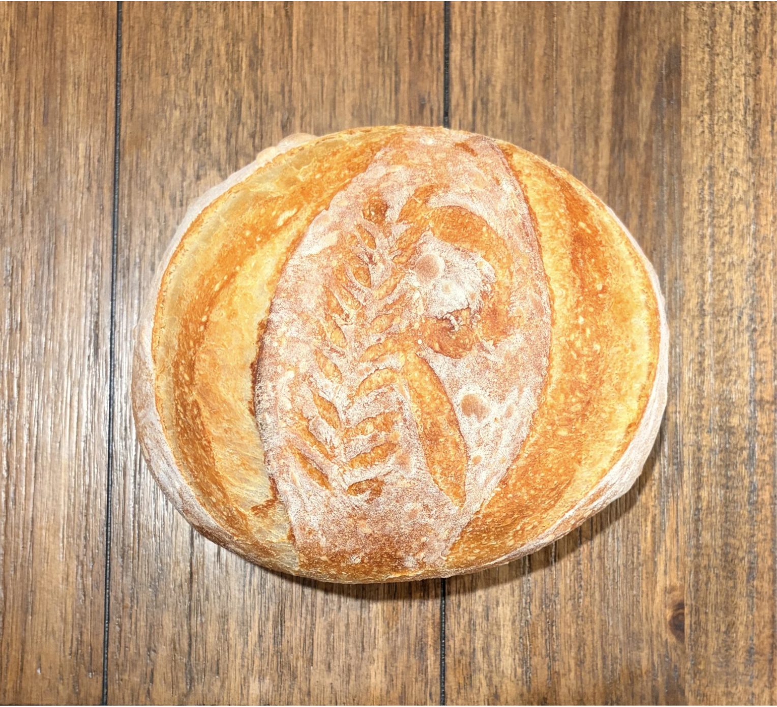 A round loaf of bread with a decorative imprint of a carrot and leaves on the top, resting on a wooden surface.