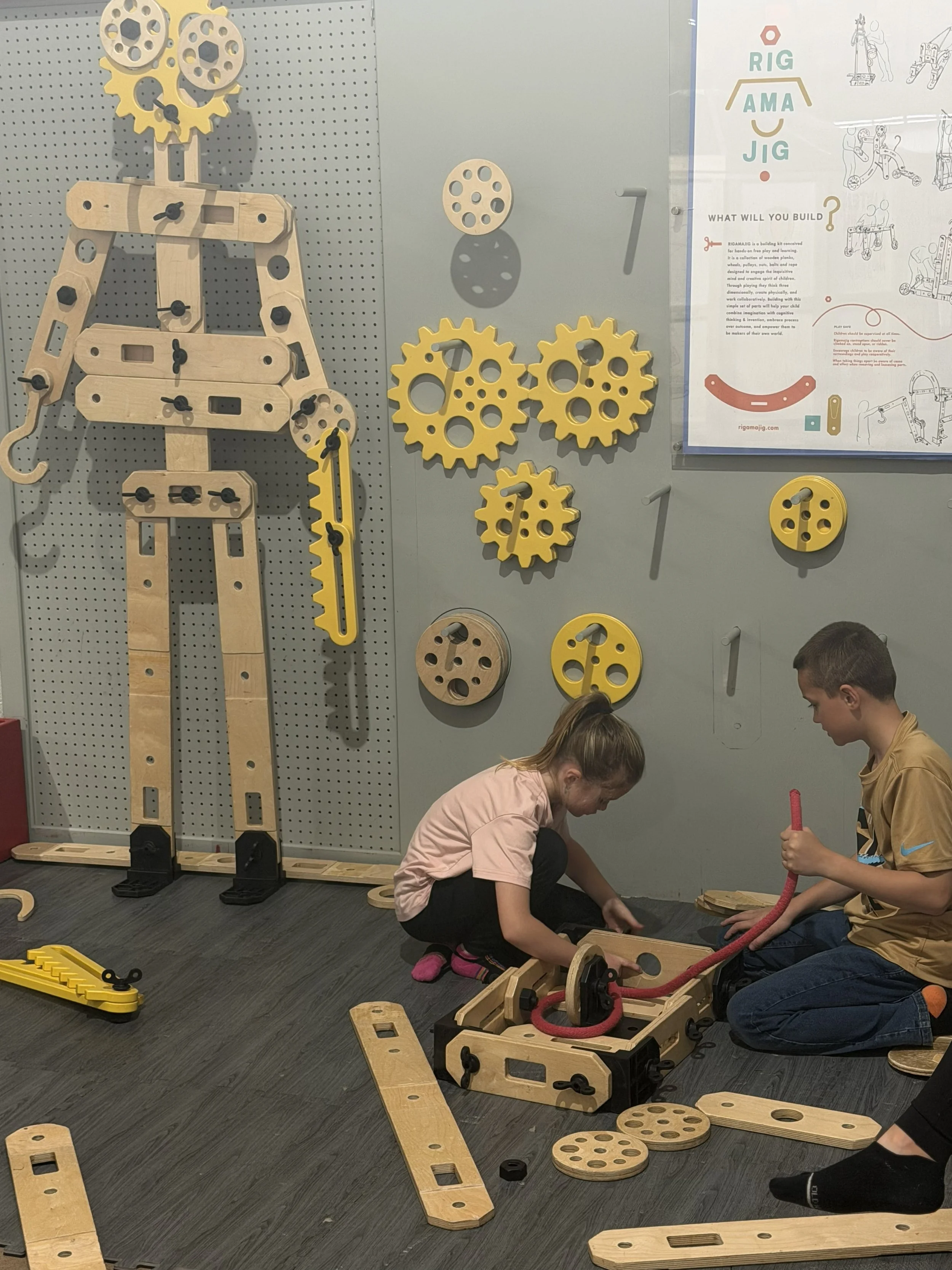 Children playing with wooden mechanical building kits at a learning exhibit.