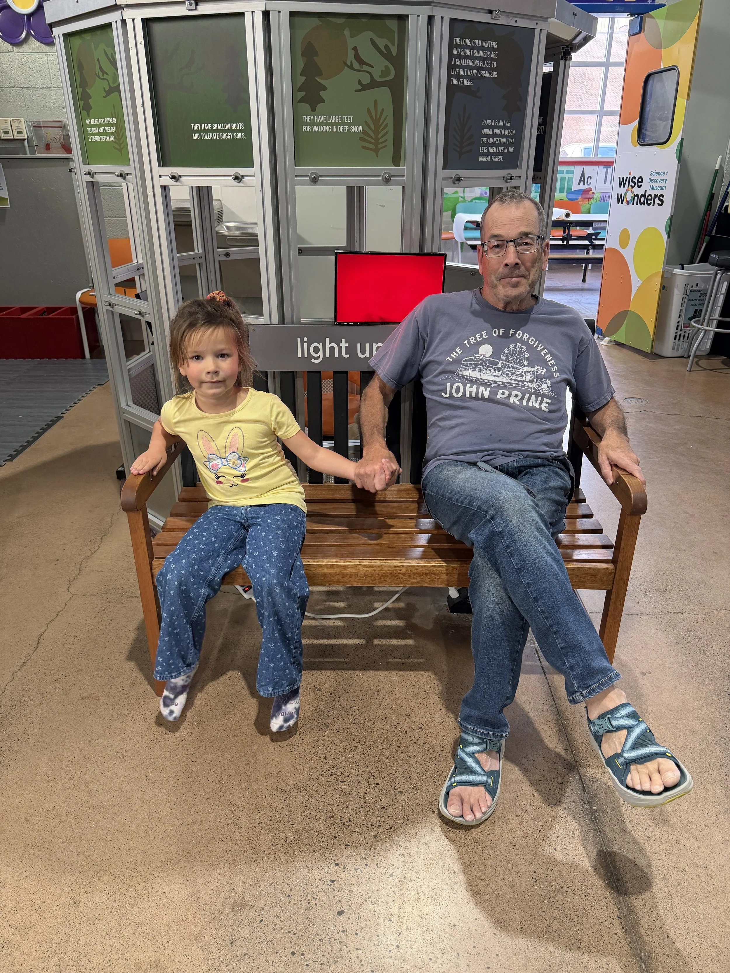 A man and a girl sitting on a wooden bench holding hands in a science museum.
