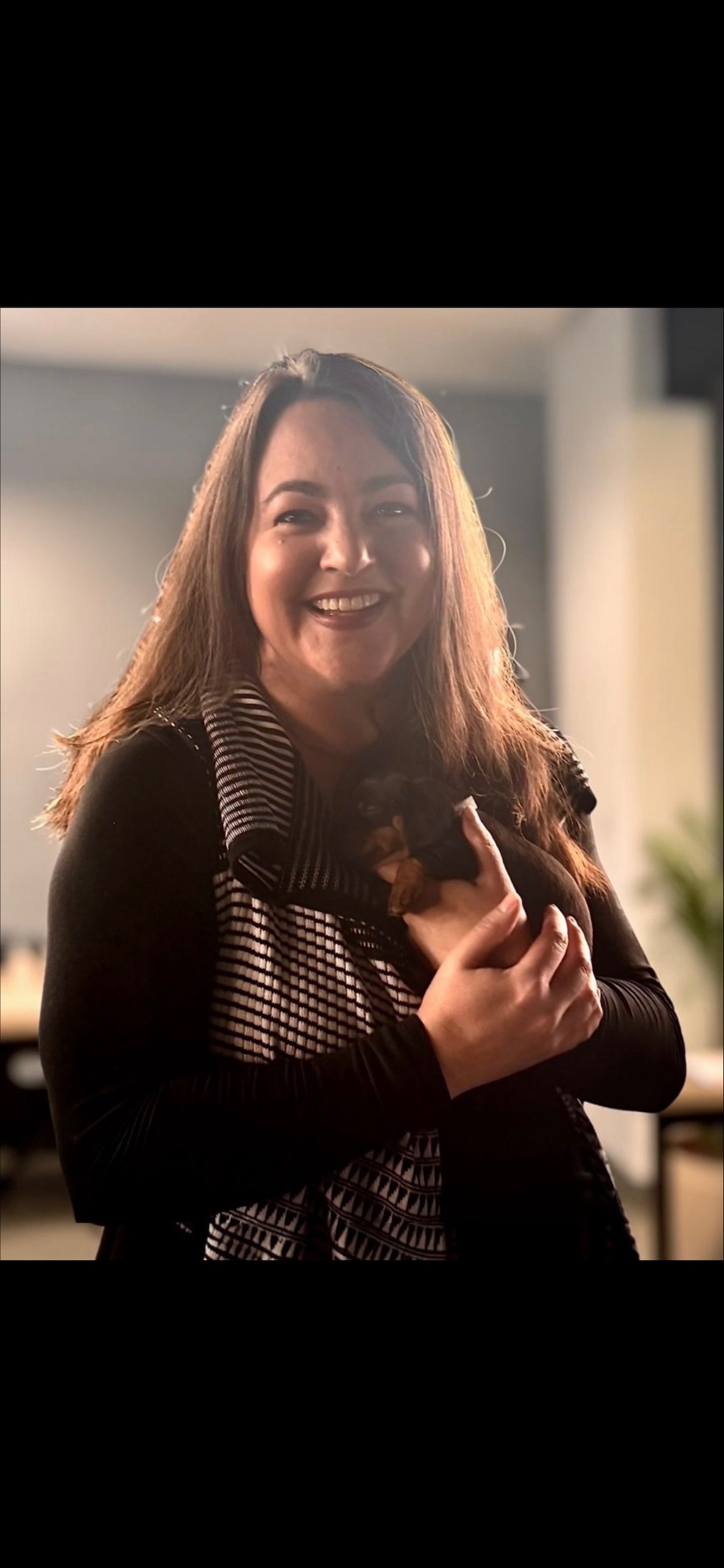 Woman smiling and holding a small puppy indoors.
