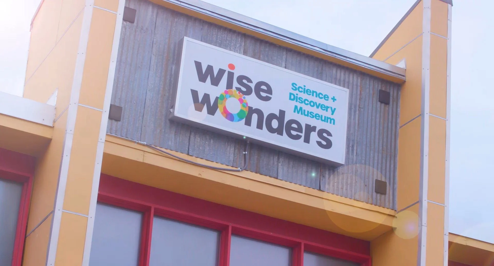 Exterior of the Science + Discovery Museum with a sign reading 'Wise Wonders' featuring colorful circular graphics.