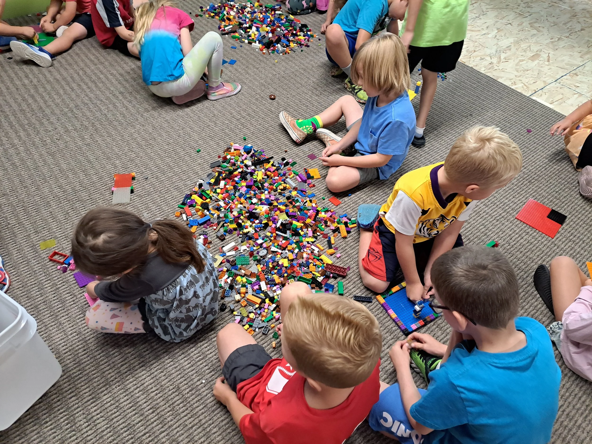 Children playing with and building with scattered Lego bricks and pieces on a carpeted floor.