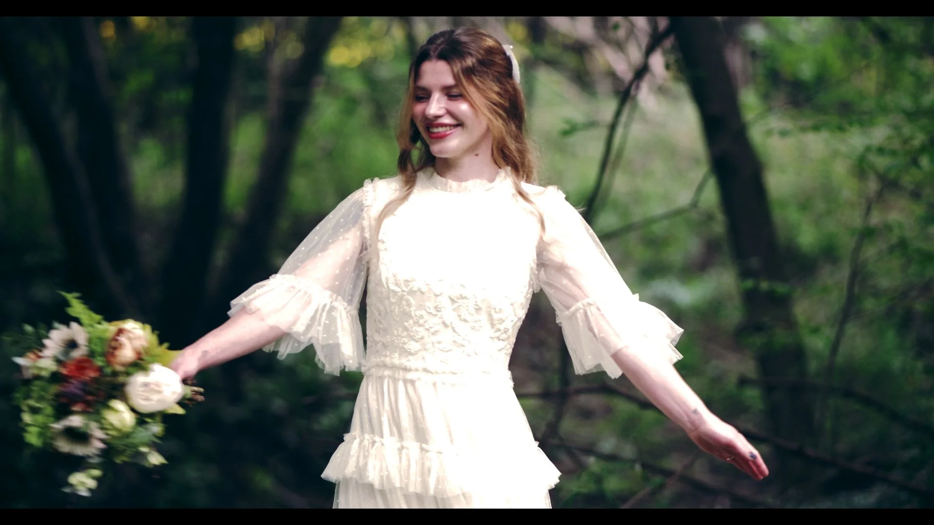 A woman in a cream lace dress holding a bouquet of flowers in a forest.