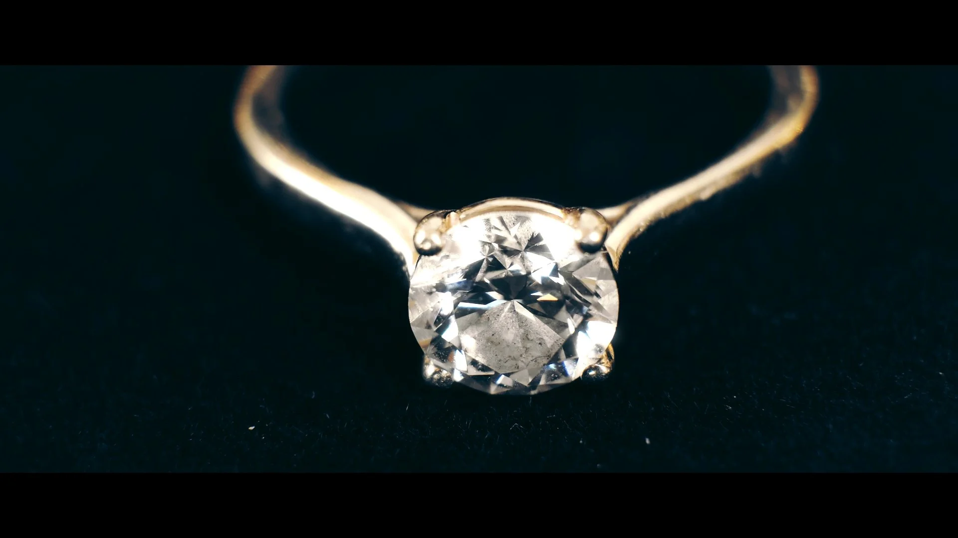 Close-up of a diamond solitaire ring with a round-cut diamond mounted on a gold band on a dark background.