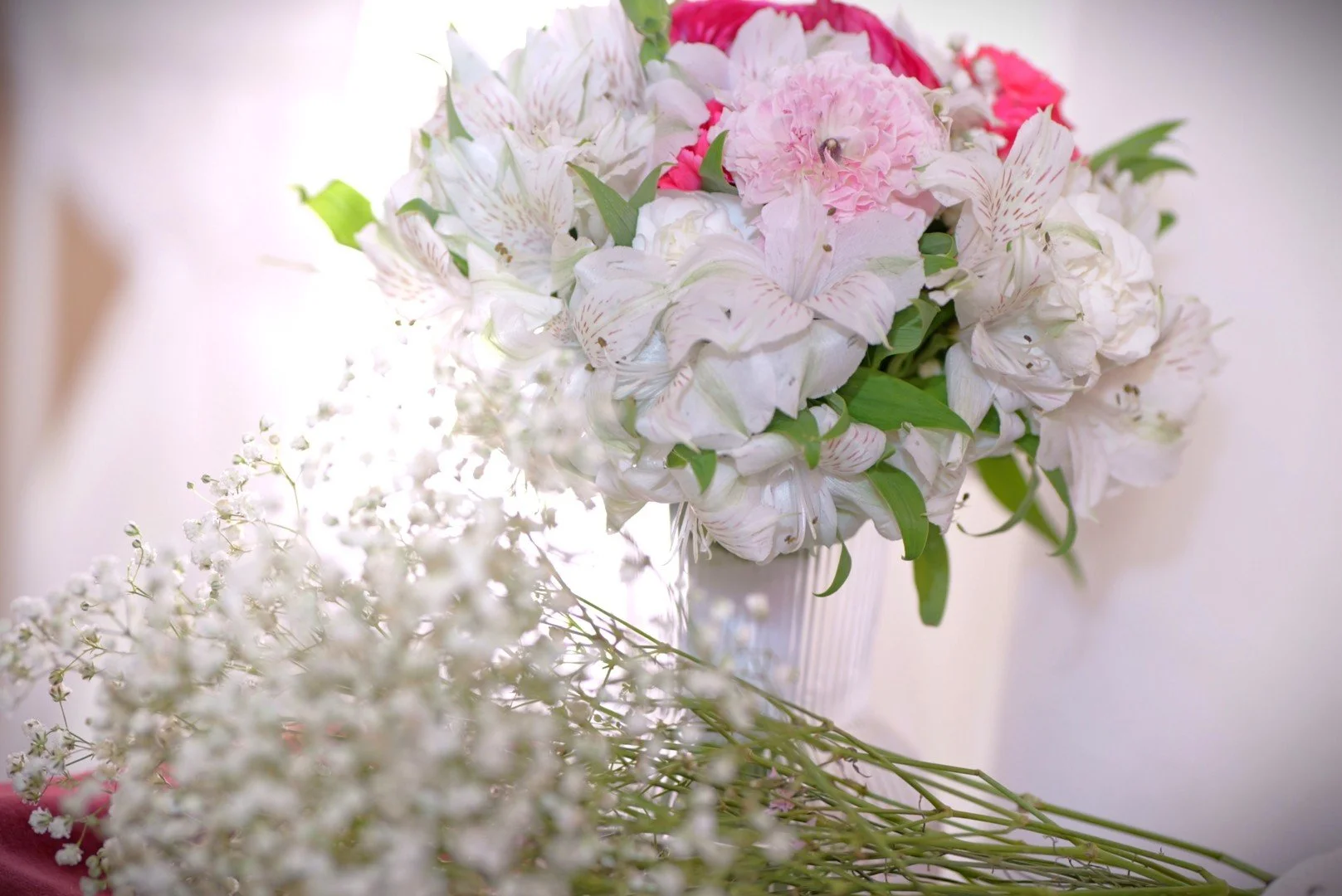 A close-up of a bouquet of pink, white, and green flowers in a white vase, with some white and pink flowers resting beside it.