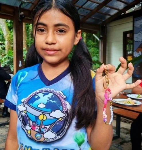 Young girl with long dark hair holding a pink and clear beaded bracelet in an outdoor patio setting.