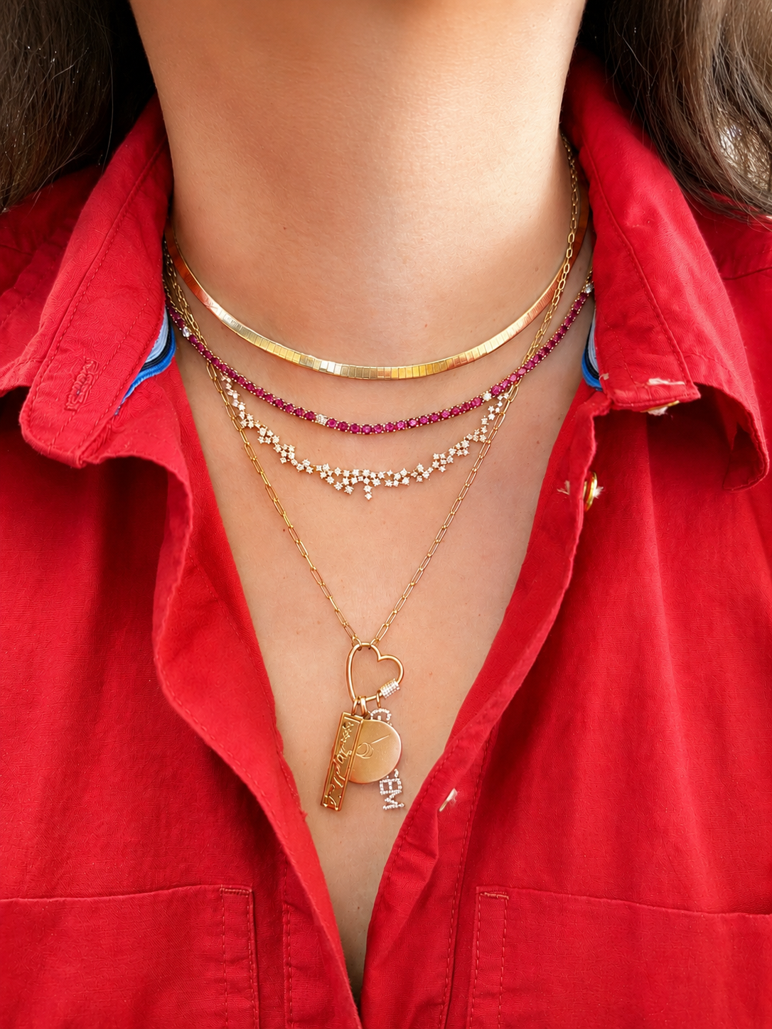 Close-up of a person's neck and chest showing four layered necklaces and a red shirt with a collar.