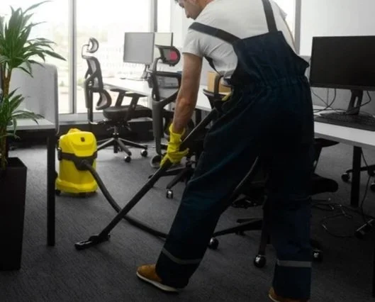 Person cleaning an office floor with a yellow wet vacuum cleaner in a modern office.