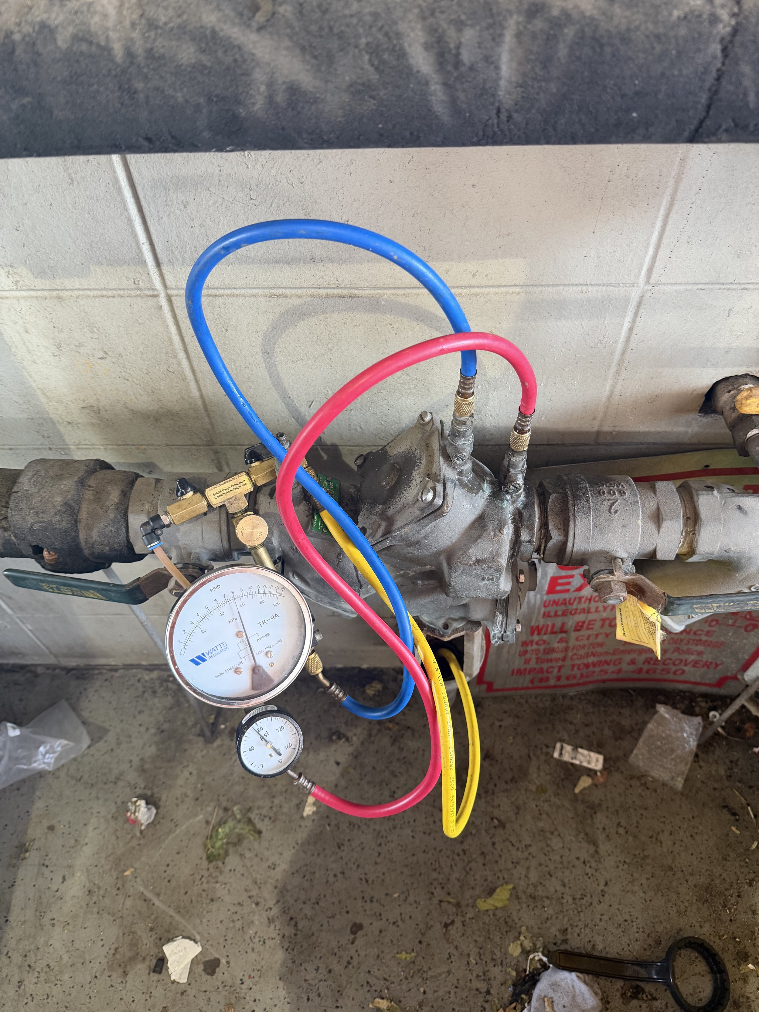 Close-up of a mechanical device with gauges and colored hoses, set against a concrete wall and floor.