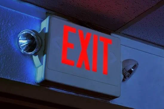 Red illuminated EXIT sign mounted on a wall with blue lighting.