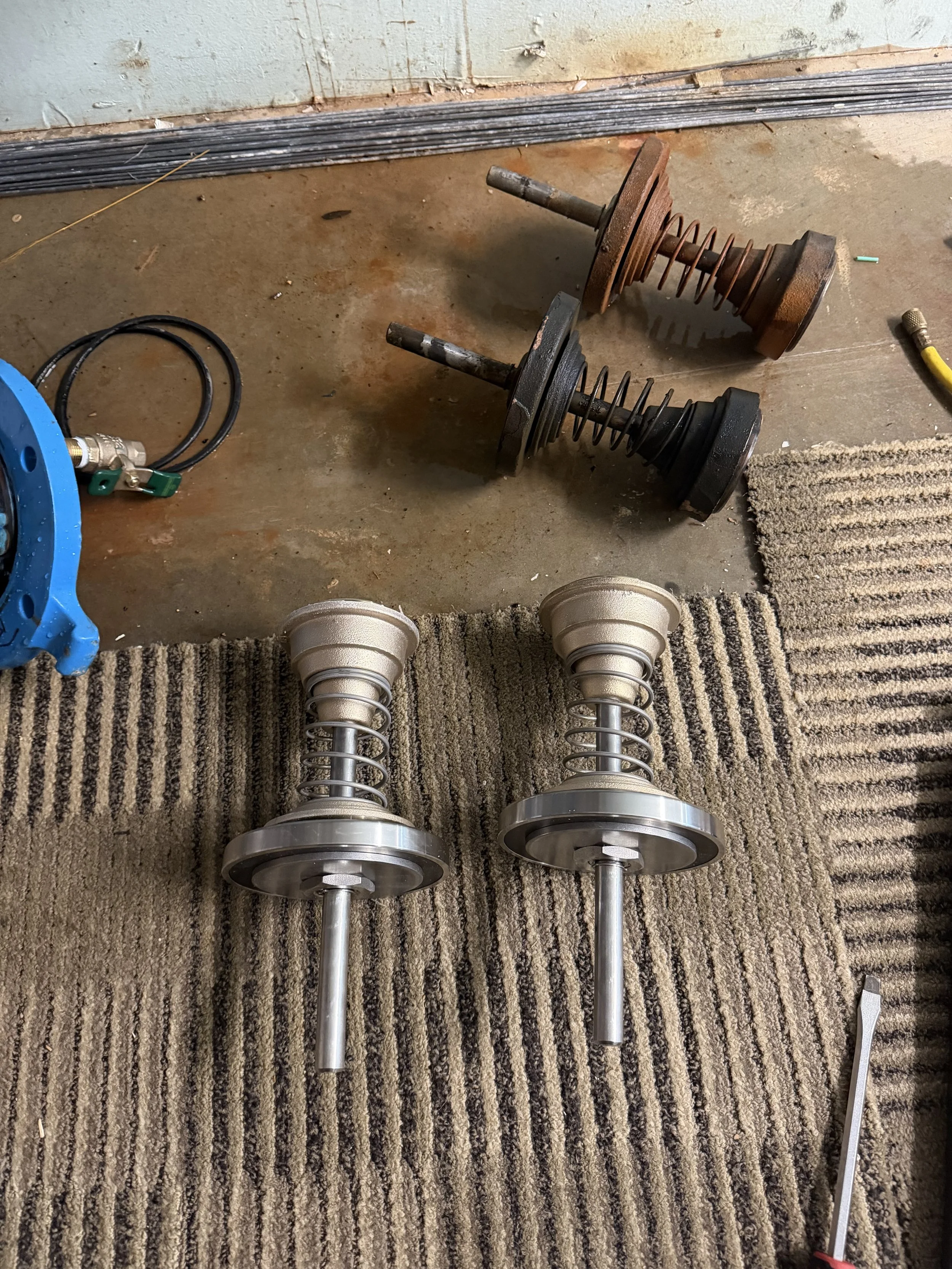 Two automotive shock absorbers with coil springs, laying on a carpeted surface next to a pair of light bulbs.