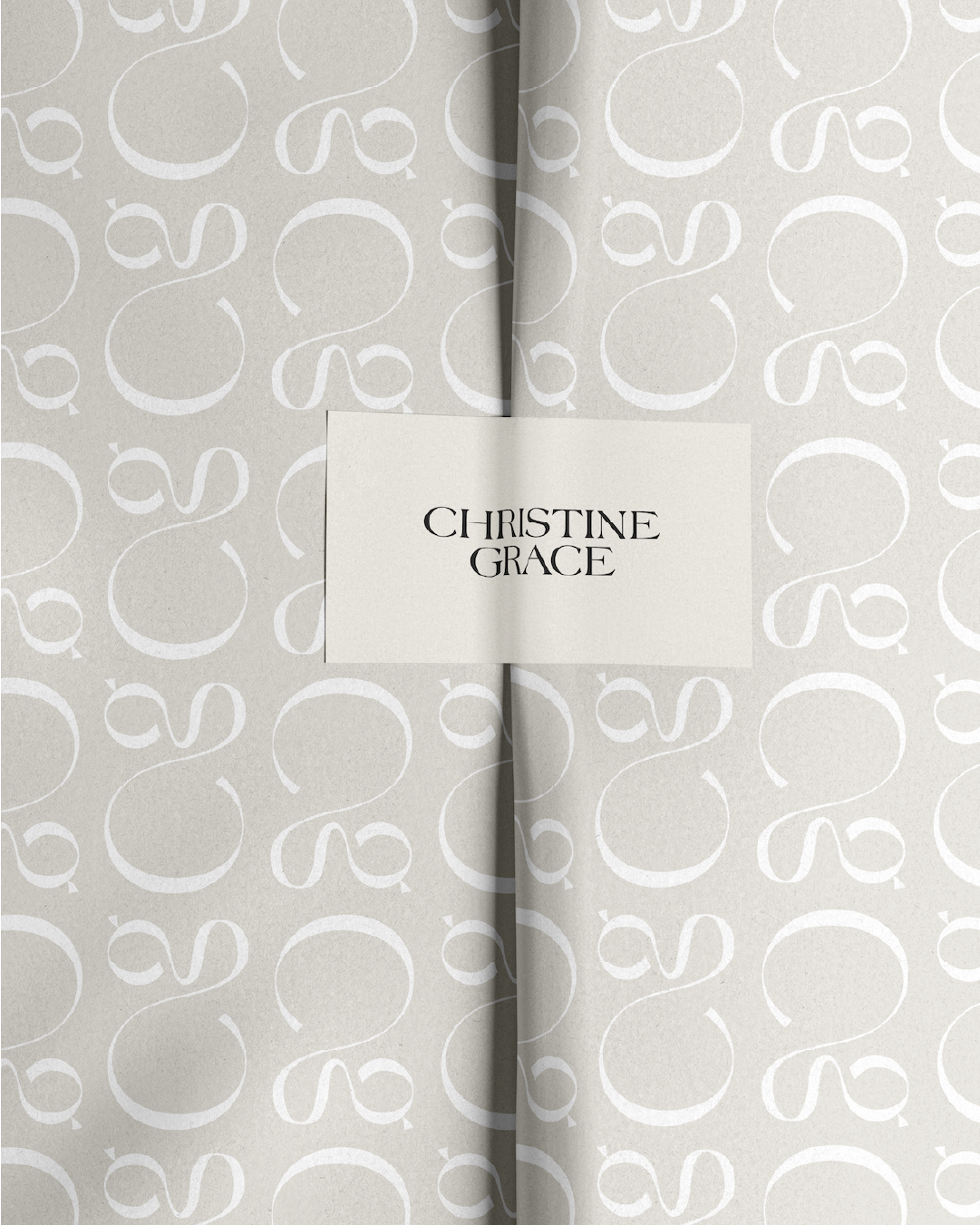 A white branded sticker with the Christine Grace logo in black acting as a closure on a branded patterned tissue paper featuring white CG logo in a repeating pattern.